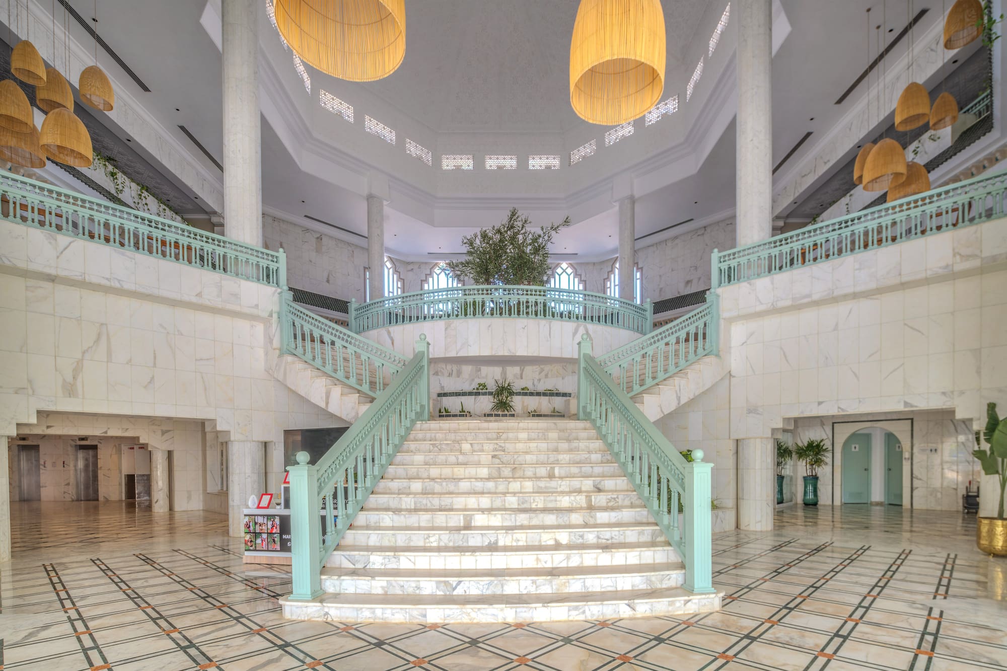 Grand hotel atrium with marble staircase and mint green railings.