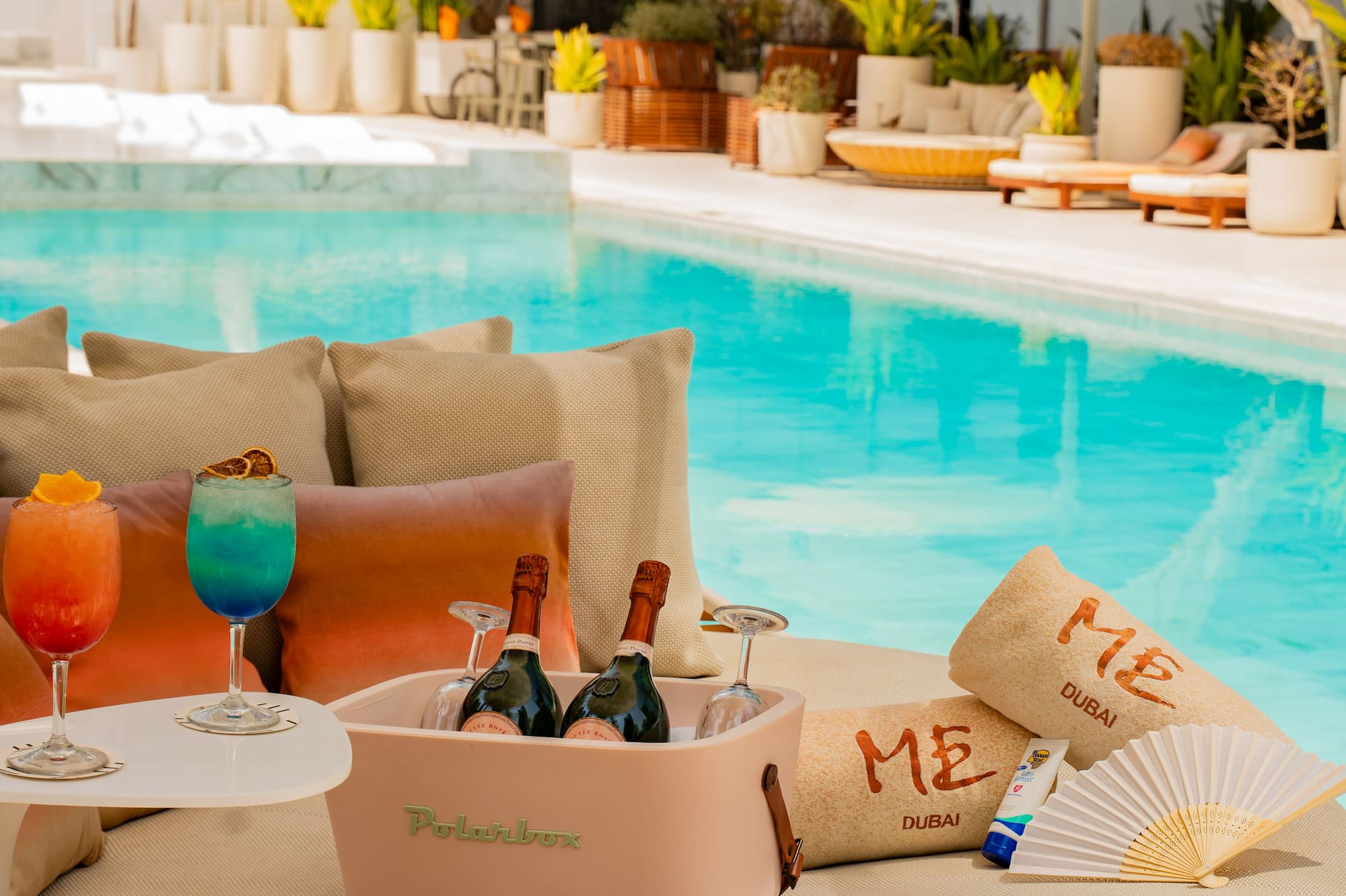 Dubai luxury poolside: cocktails, champagne cooler, ME towels on a daybed.