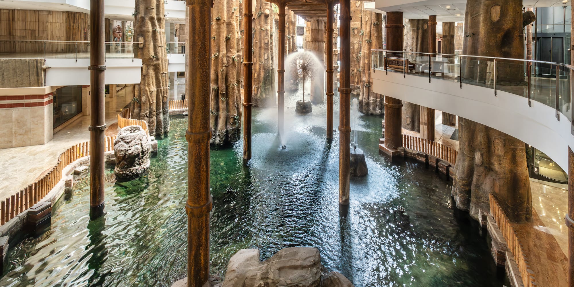 Indoor tropical atrium with large water feature, fountains, and tree-like columns.