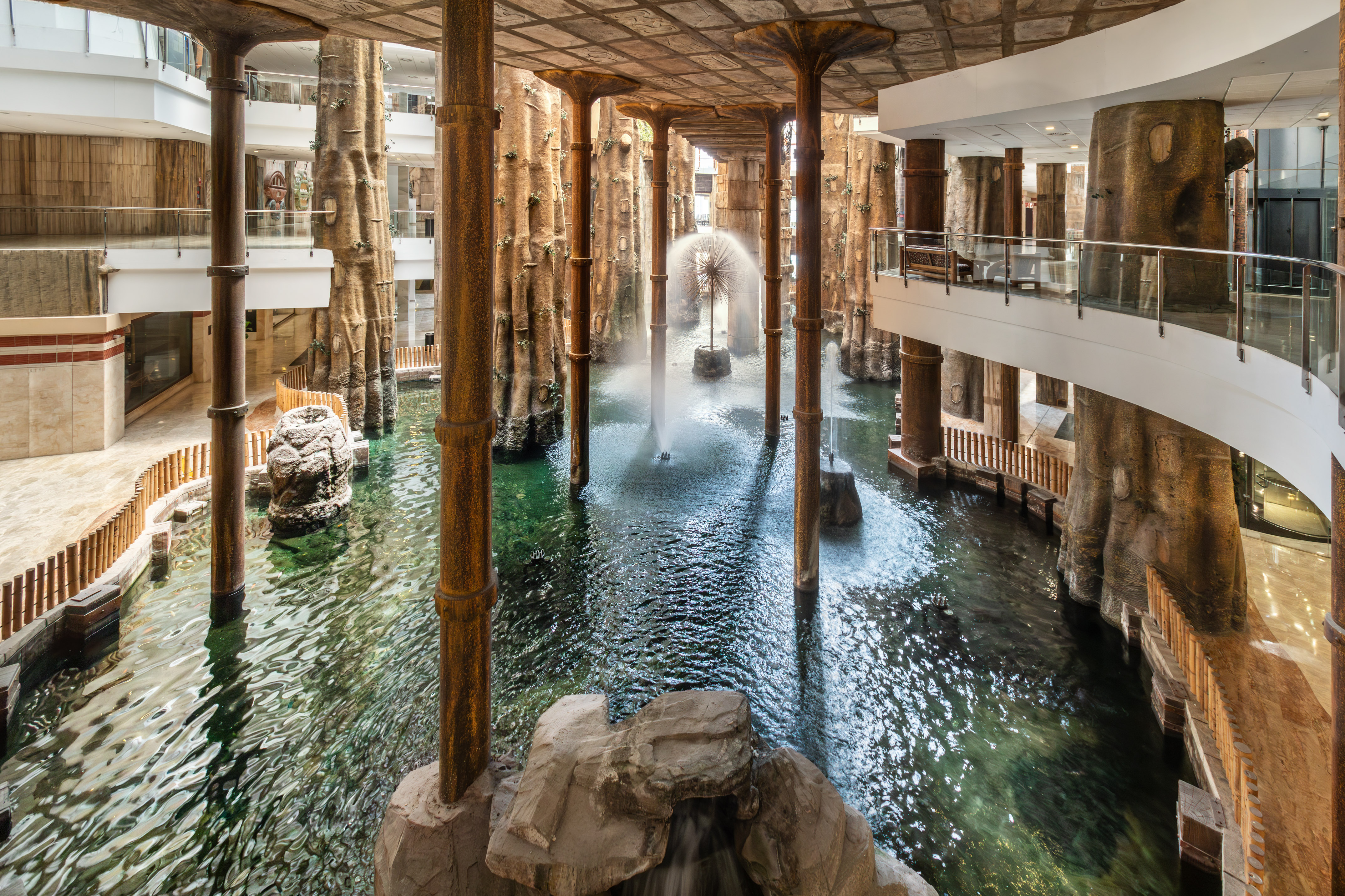 Indoor tropical atrium with large water feature, fountains, and tree-like columns.