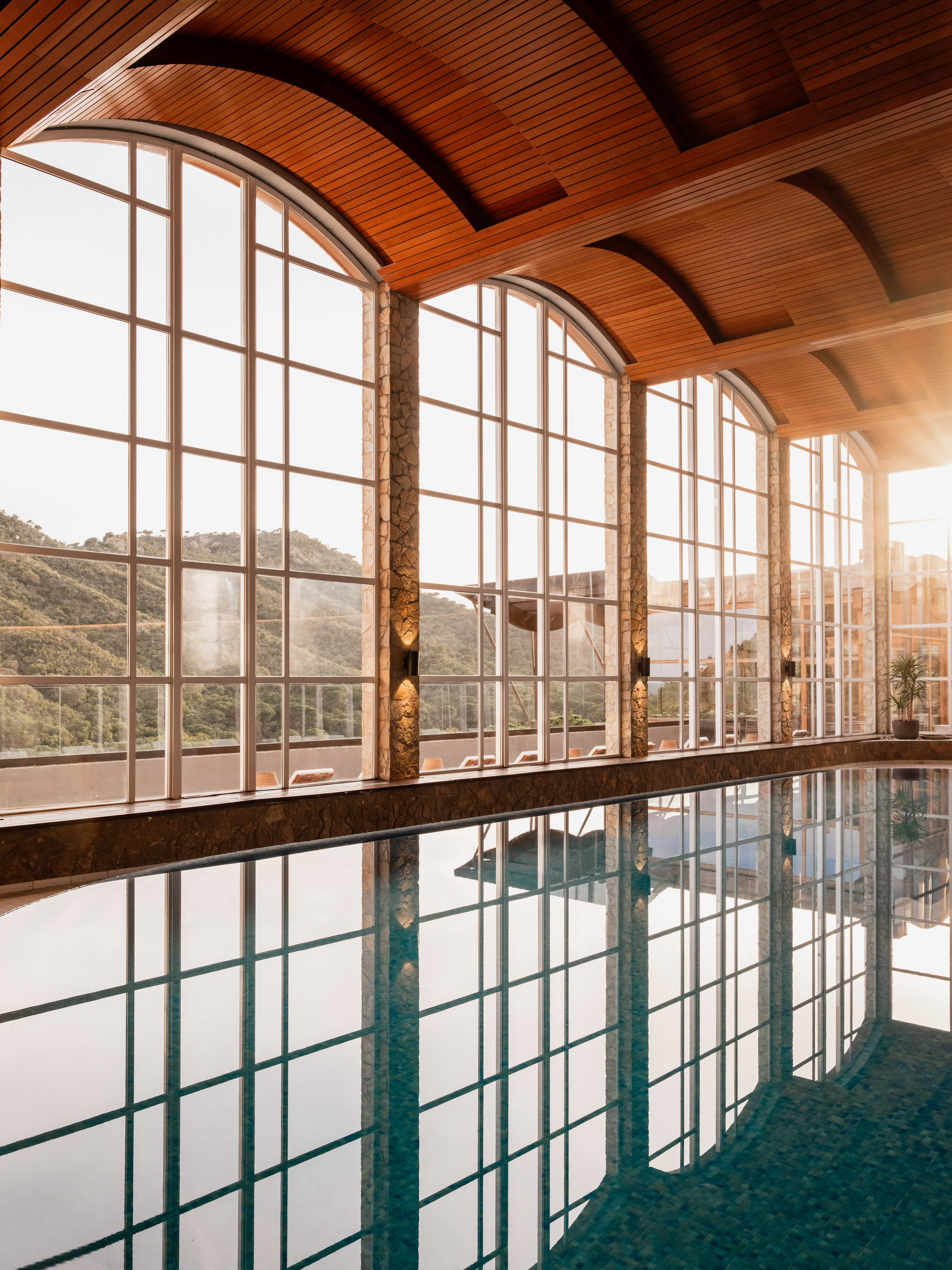 Indoor pool with panoramic mountain views, arched windows, and wooden ceiling.