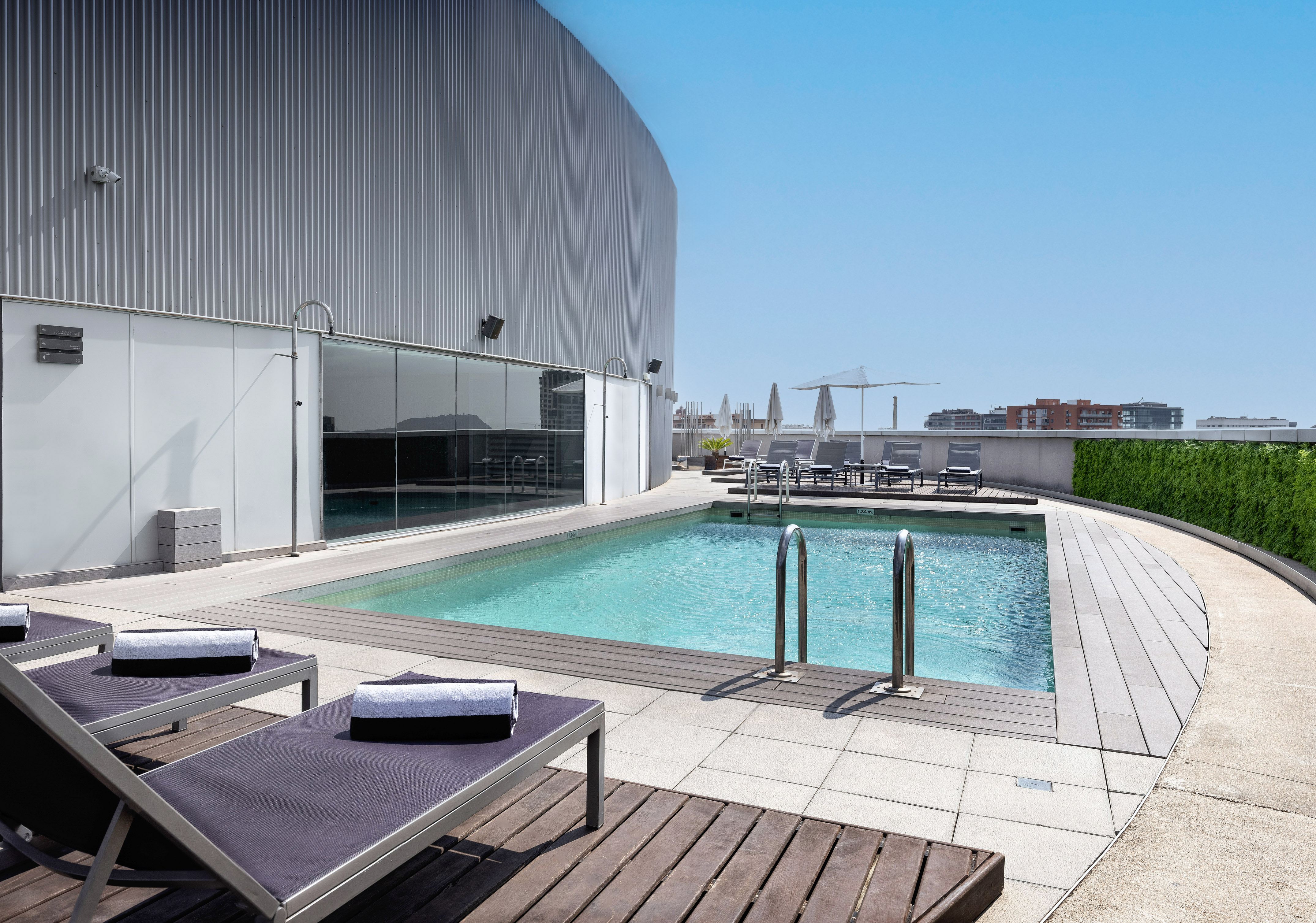 Rooftop pool with sun loungers, modern building, and clear blue sky.