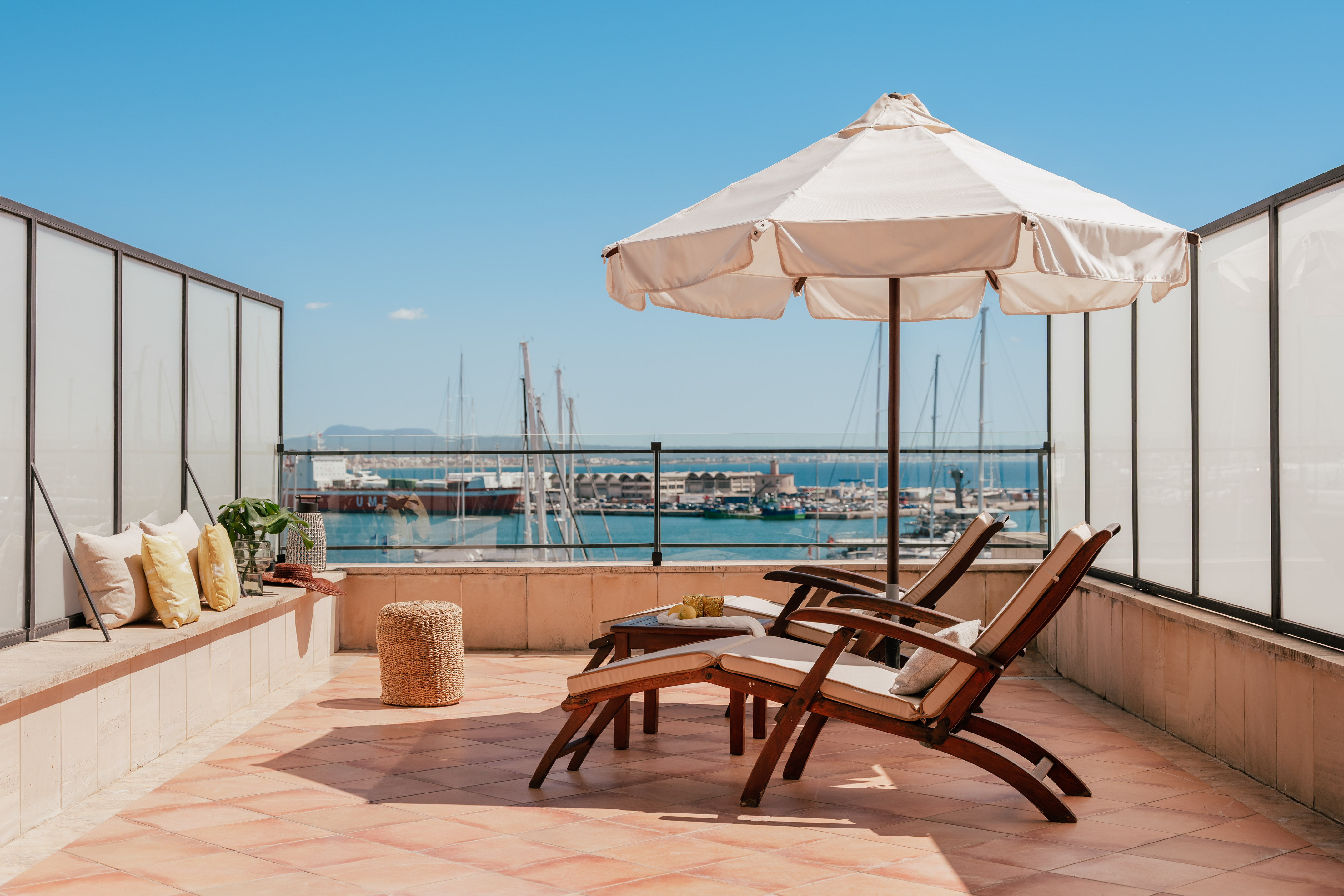 Sunny rooftop terrace with harbor view, lounge chairs, and sun umbrella.