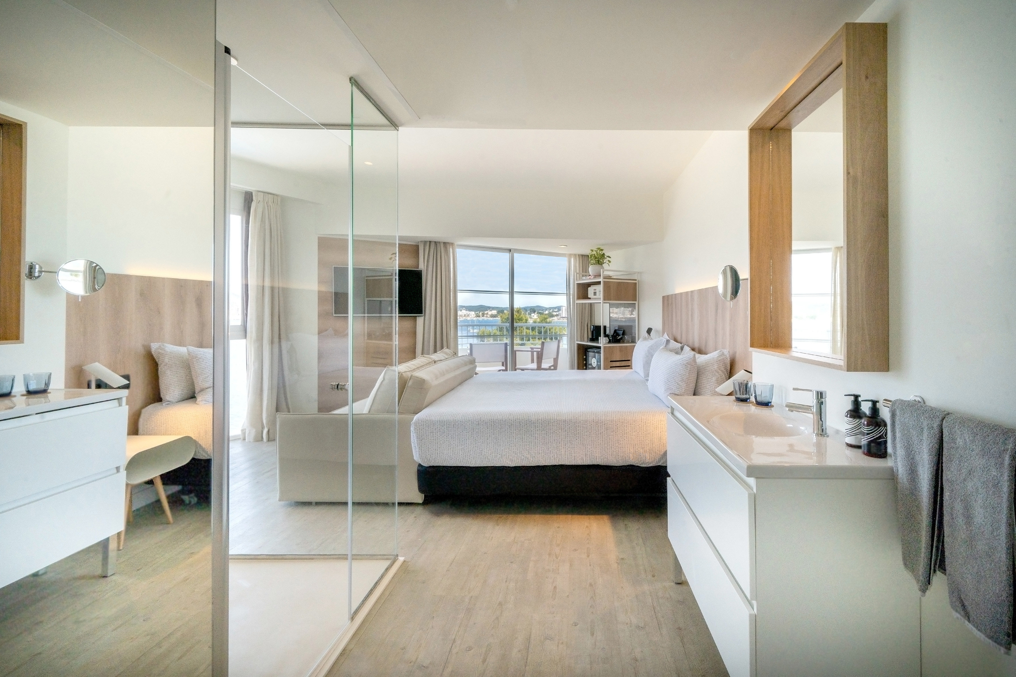 Modern hotel room with sea view balcony, king bed, and open bathroom.