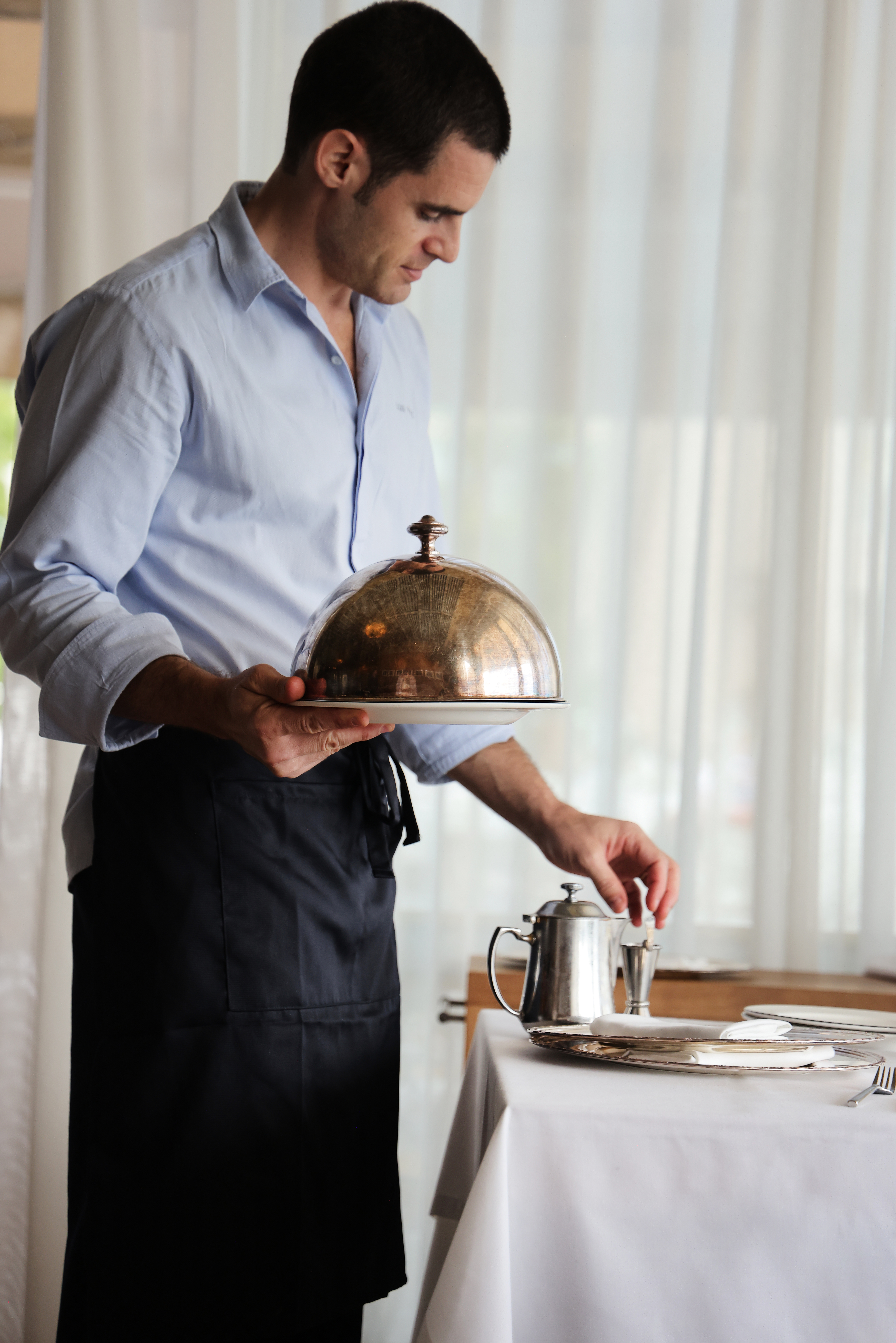 Professional waiter serving with cloche, setting a fine dining table.