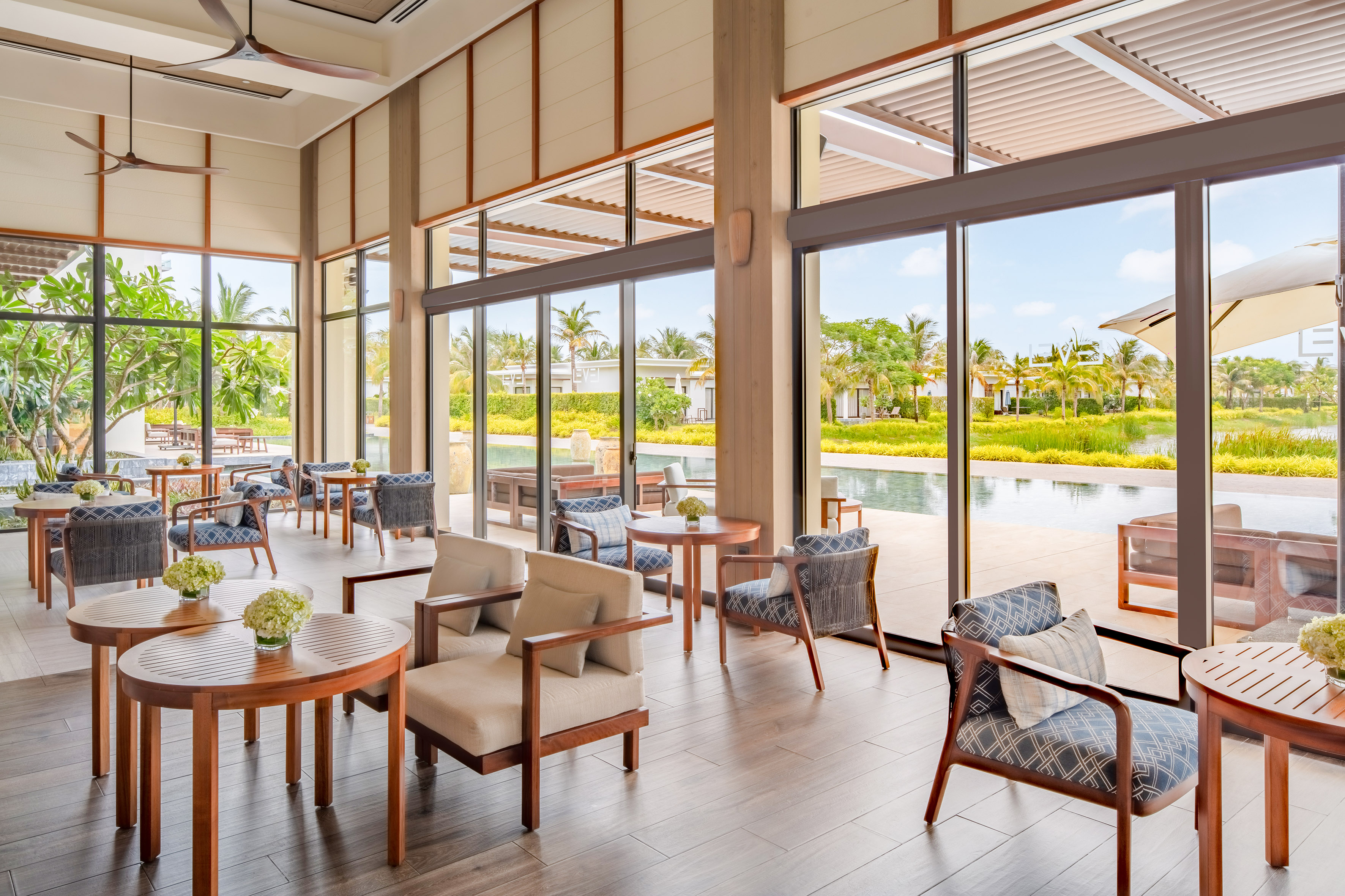 Indoor resort lounge with tropical pool and garden views, modern wood furniture.