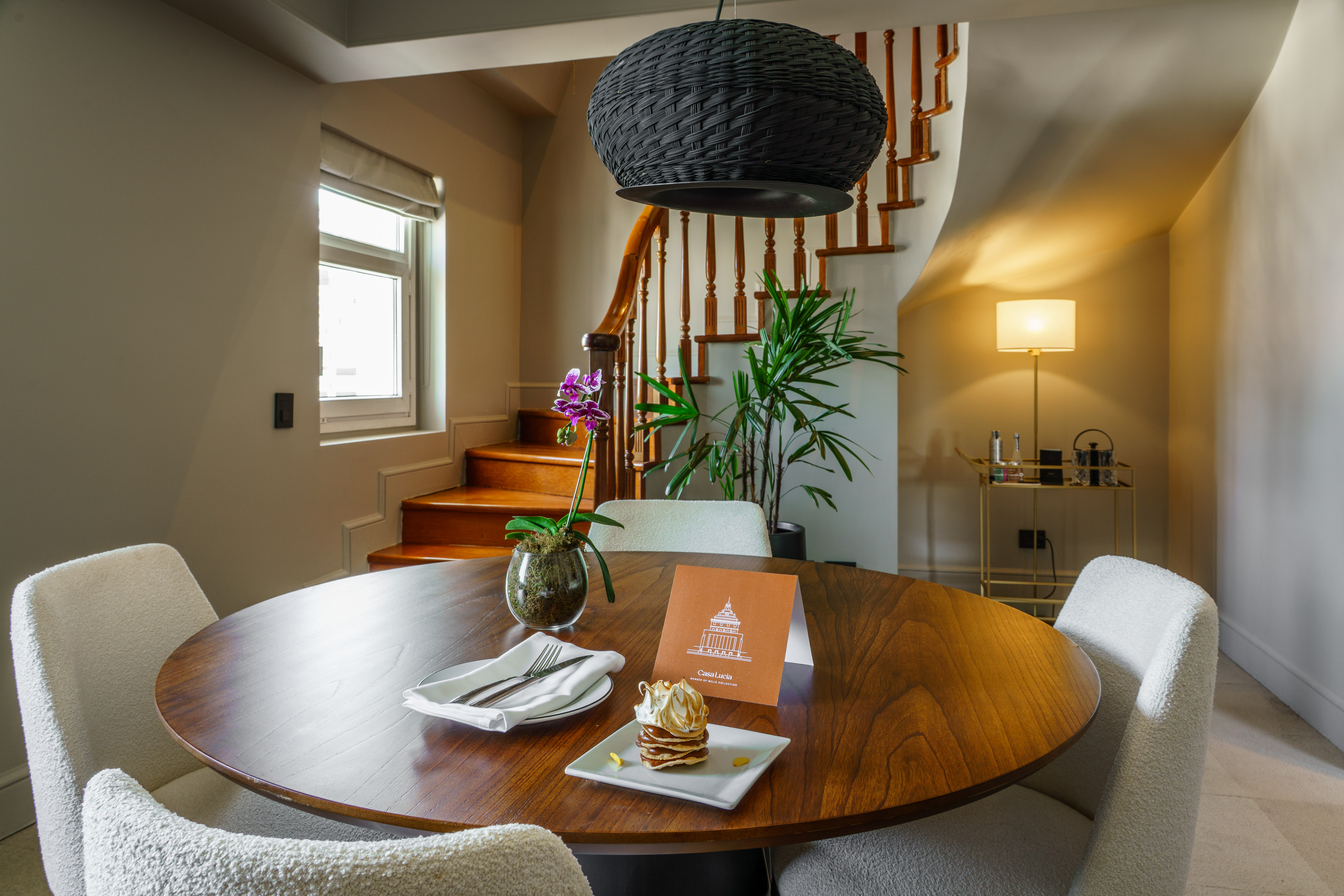 Elegant hotel dining area with round wood table, dessert, orchid, and staircase.
