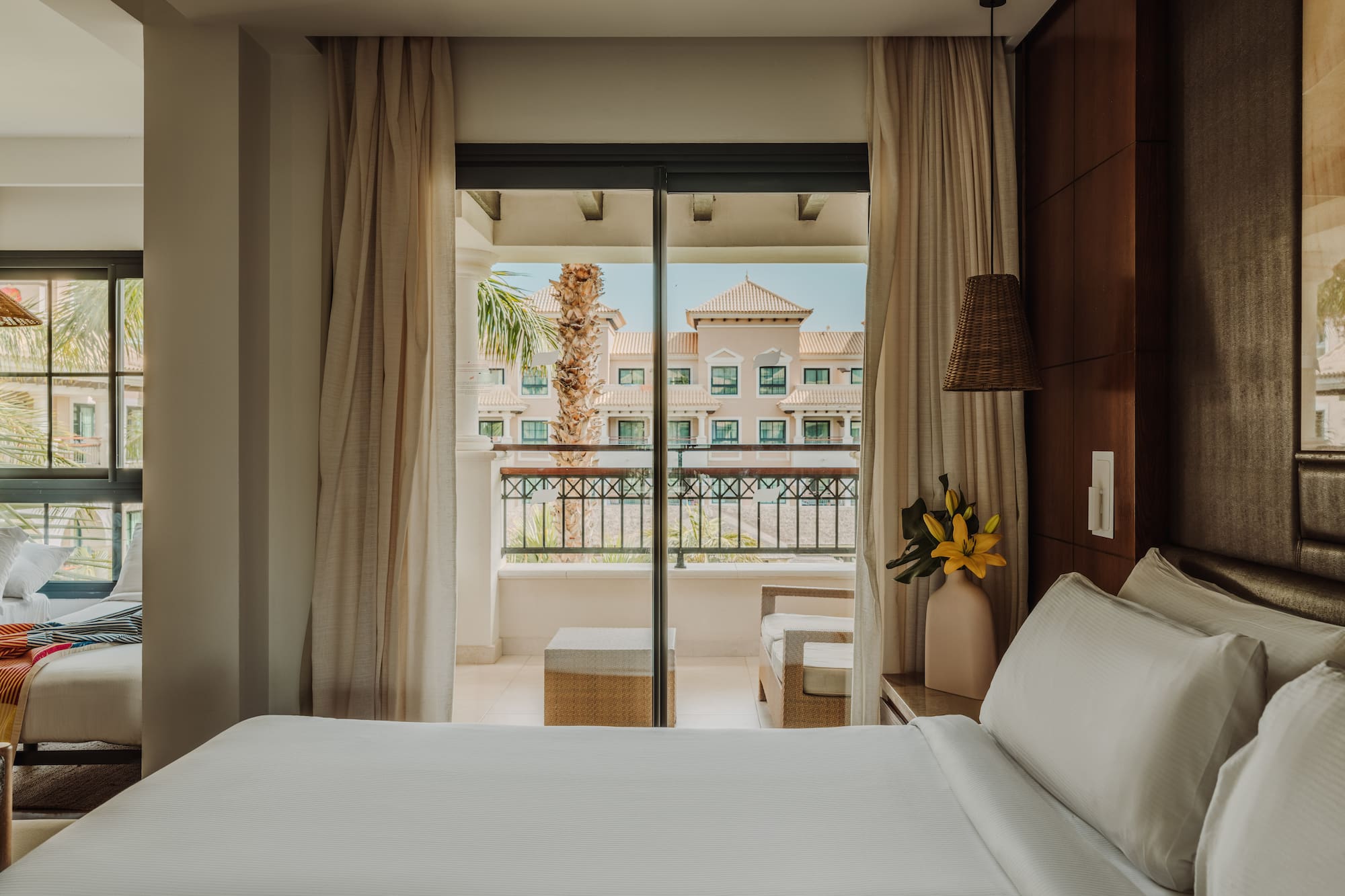 a bed with white sheets and a vase of flowers outside a glass door