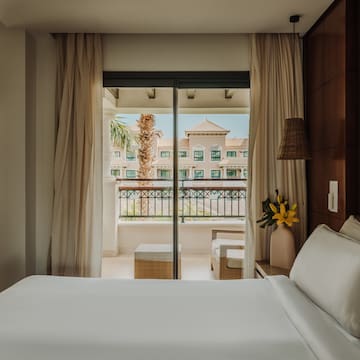a bed with white sheets and a vase of flowers outside a glass door