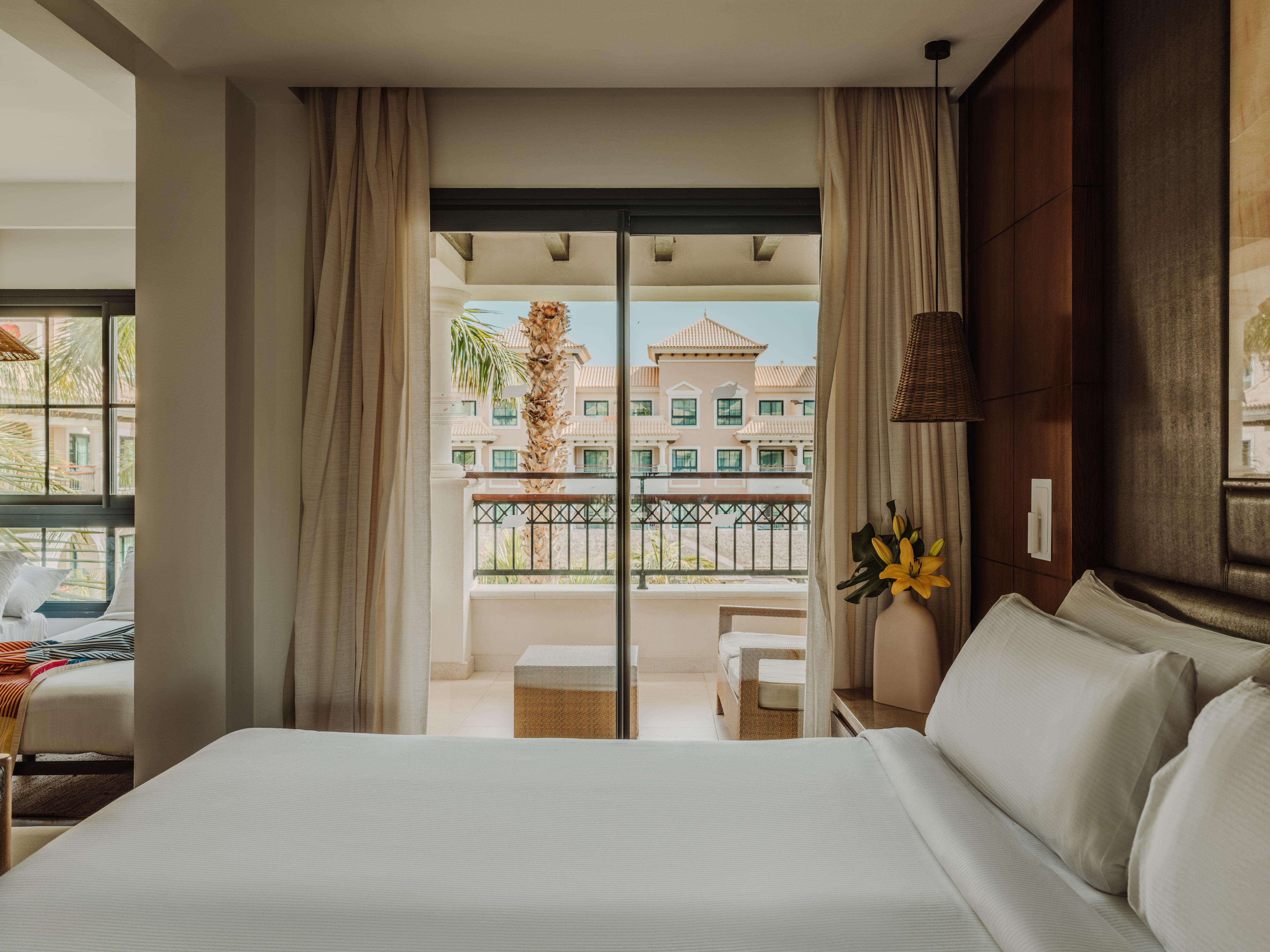 a bed with white sheets and a vase of flowers outside a glass door