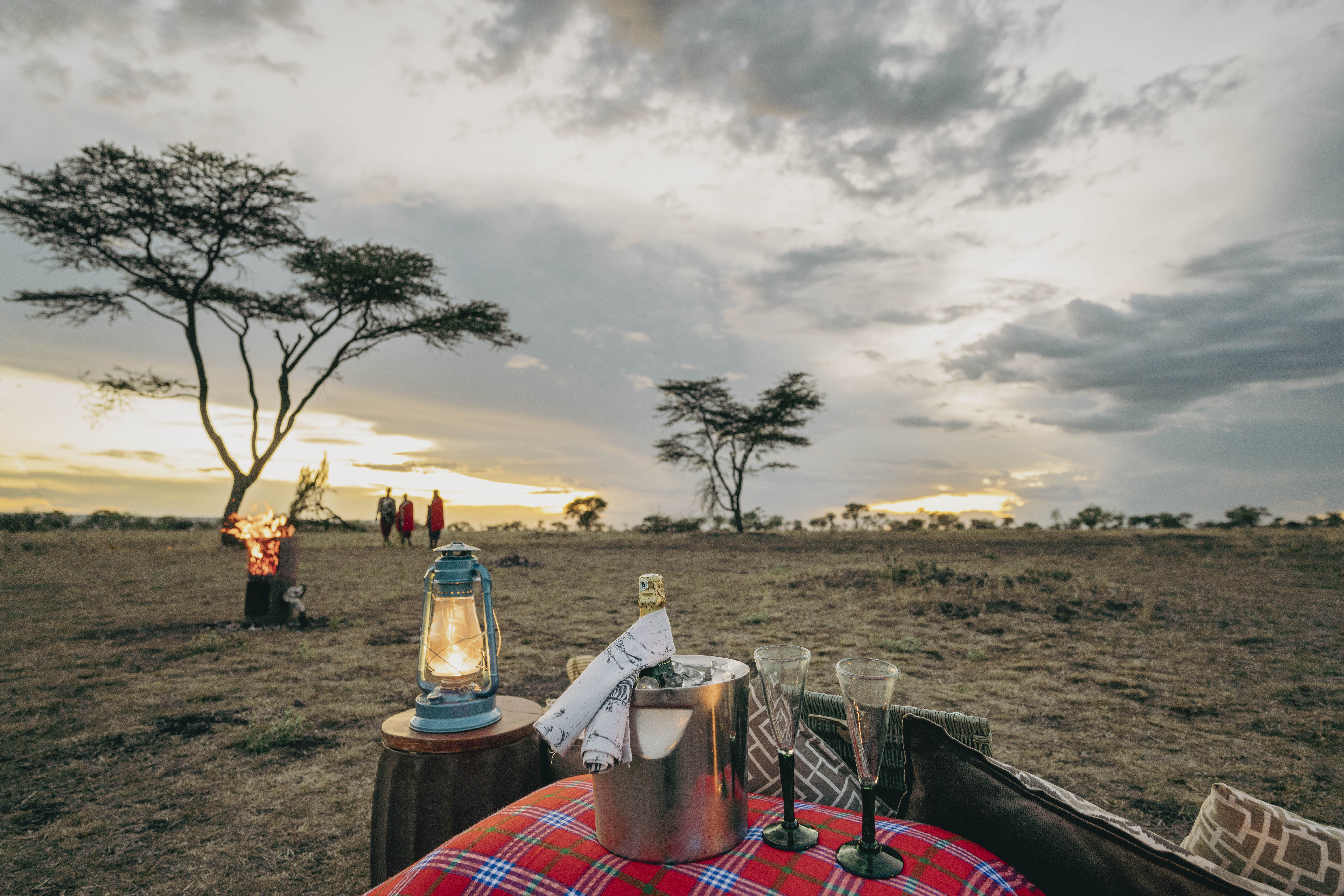 African safari sundowner: champagne, lantern, fire pit at sunset.