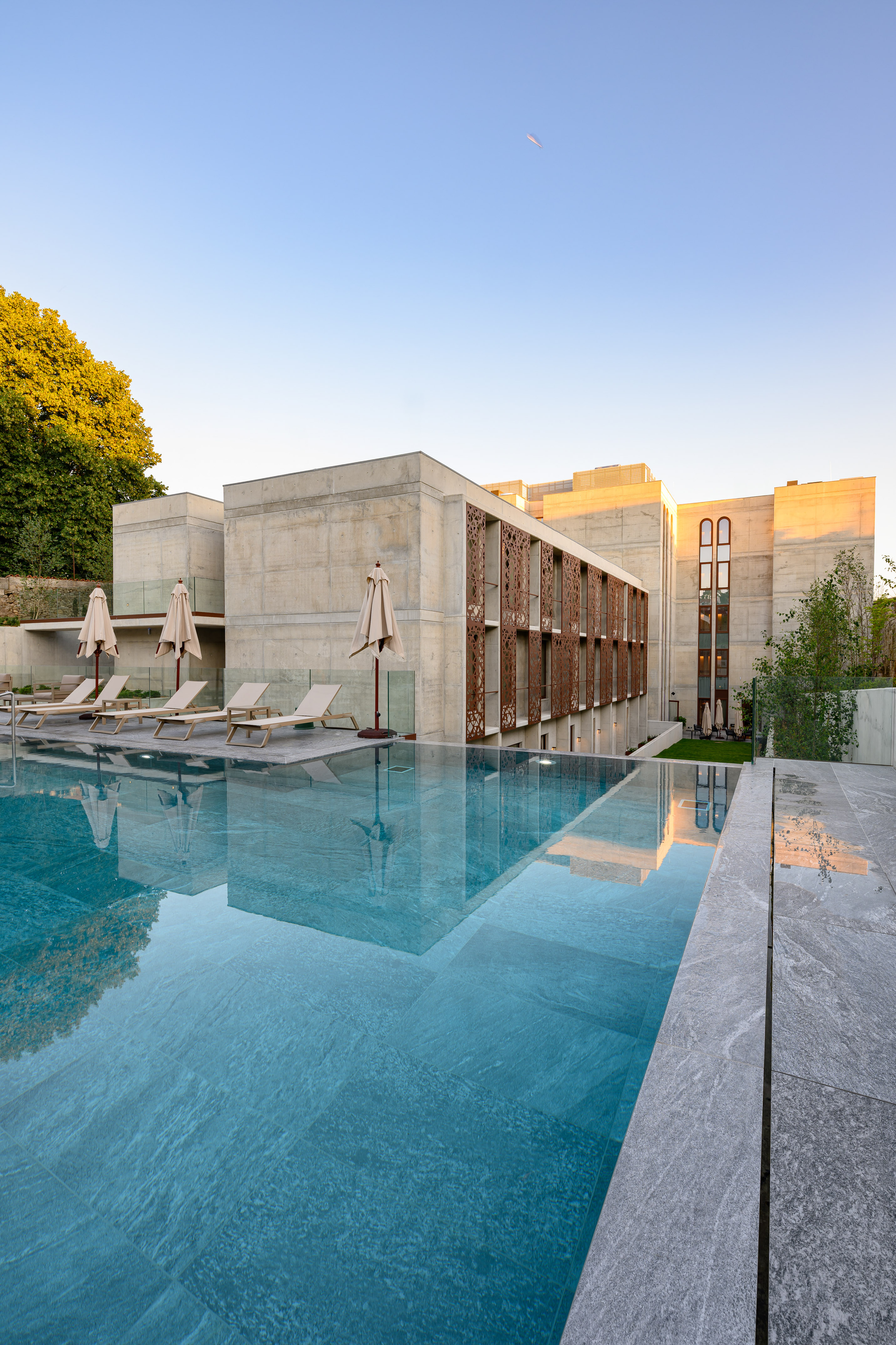 Modern concrete hotel and infinity pool with lounge chairs at sunset.