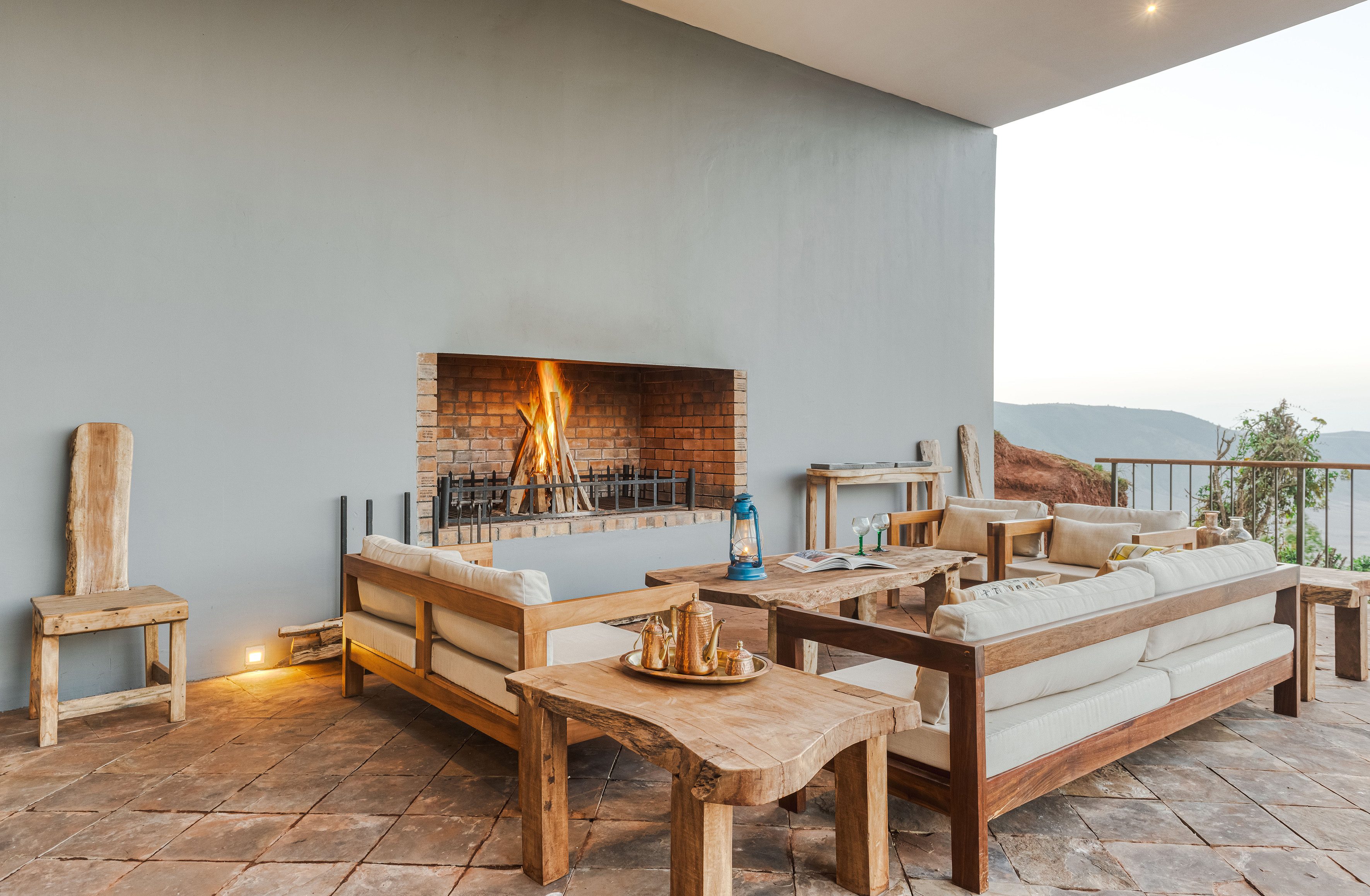 Rustic outdoor lounge with brick fireplace, wooden seating, and mountain view.