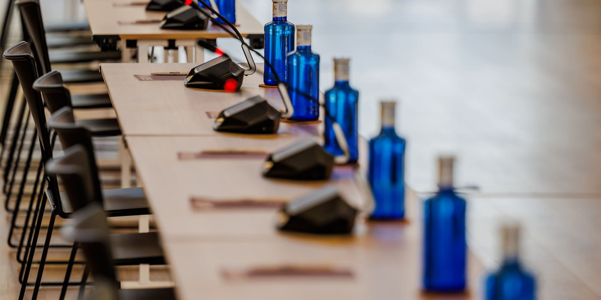 Meeting room setup: long tables, microphones, blue water bottles, chairs.