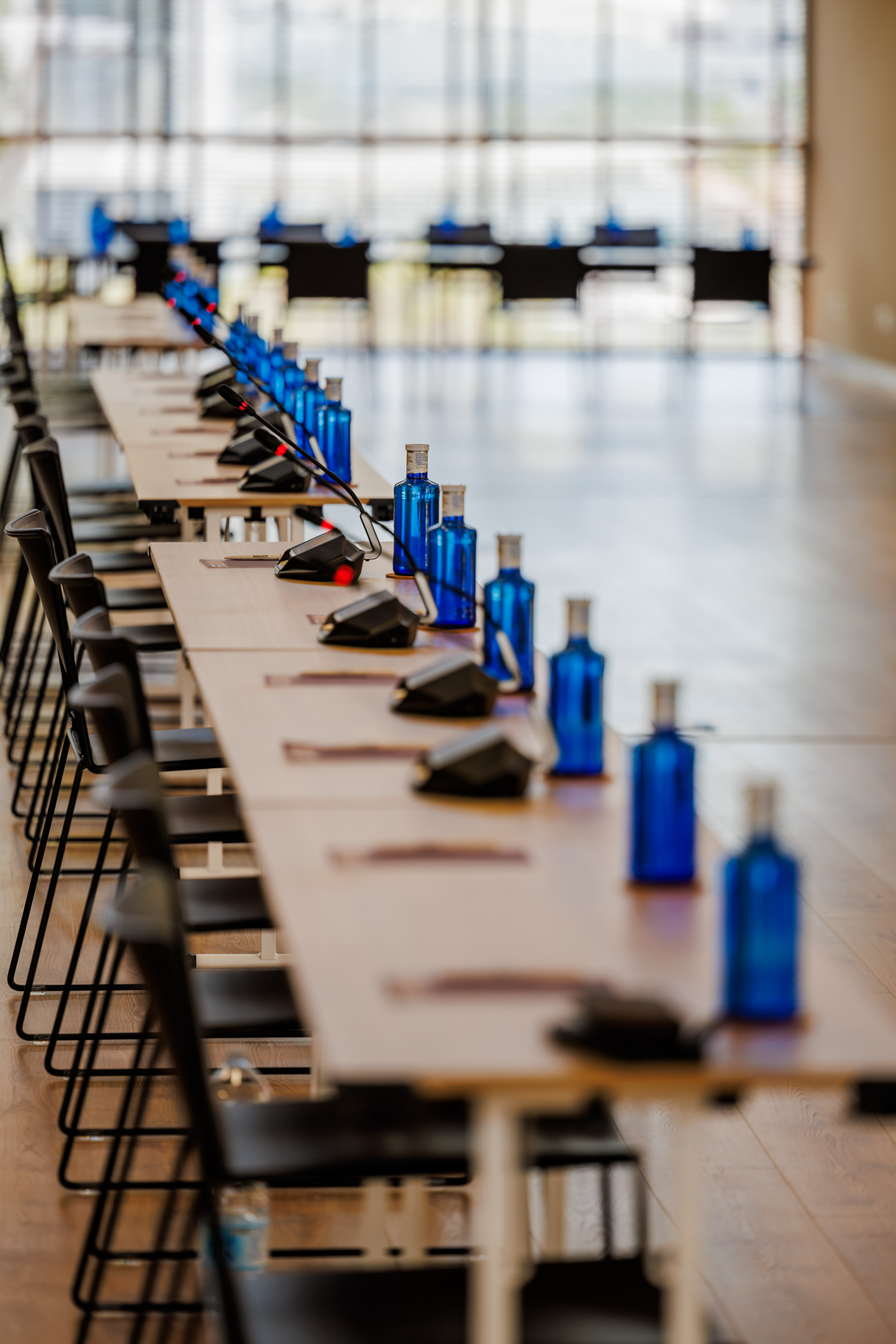 Meeting room setup: long tables, microphones, blue water bottles, chairs.