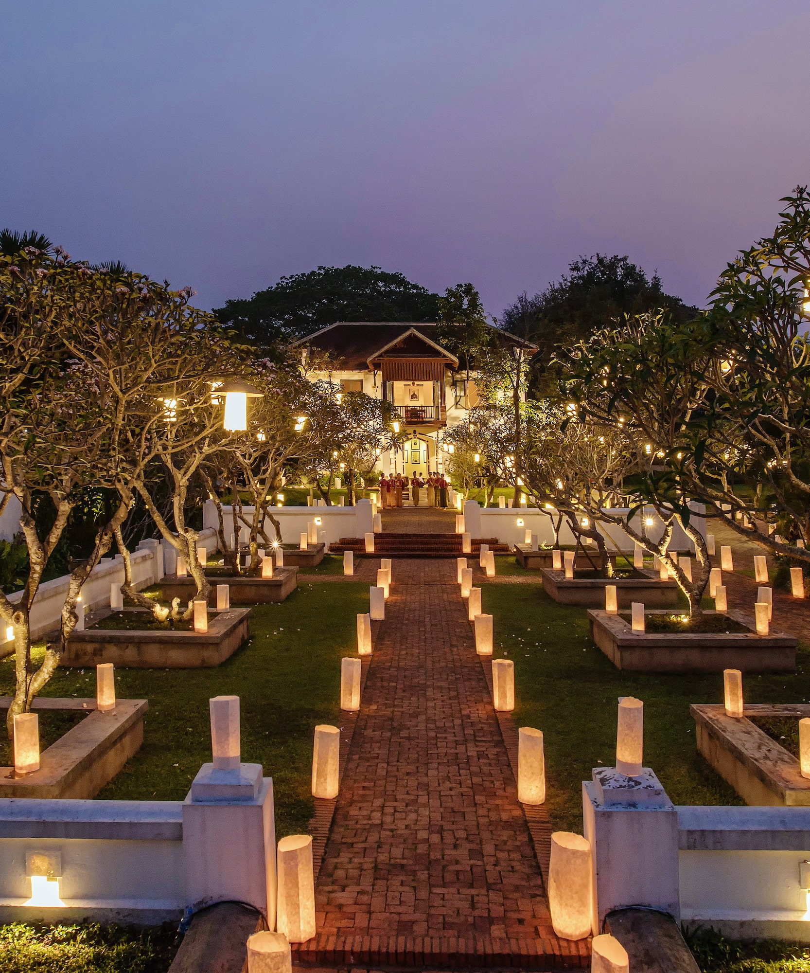 a brick path with trees and lights on it