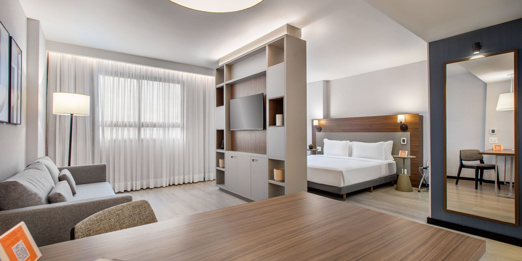 Bright modern hotel studio featuring living area, bed, and room divider with TV.