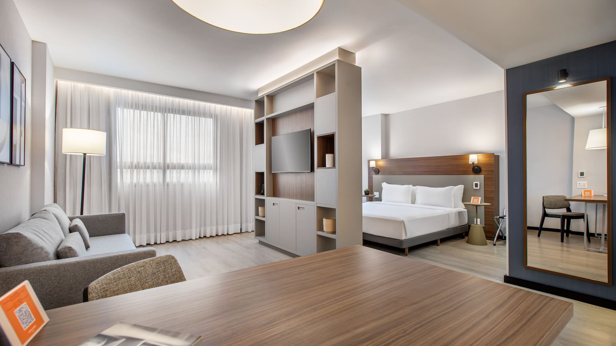 Bright modern hotel studio featuring living area, bed, and room divider with TV.