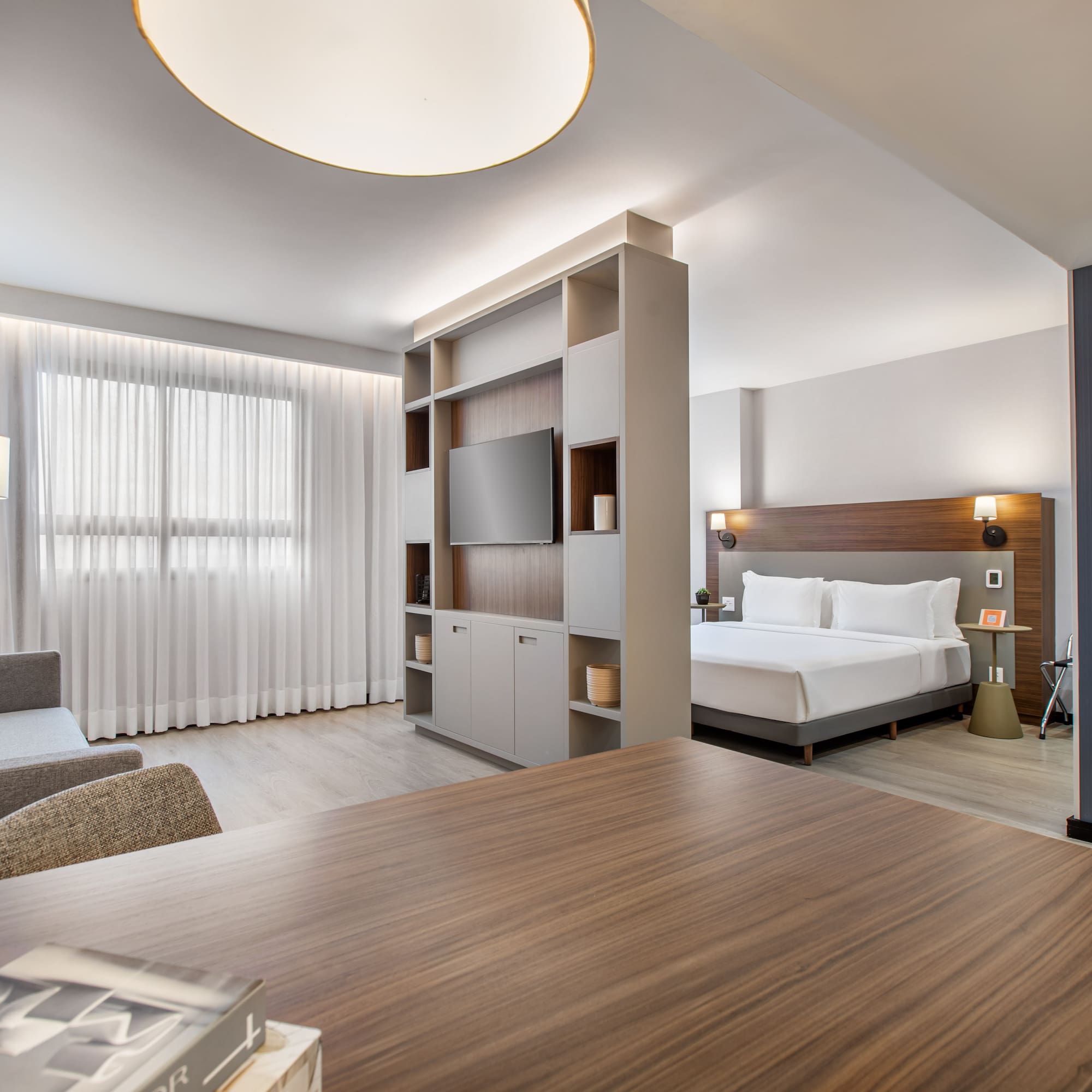 Bright modern hotel studio featuring living area, bed, and room divider with TV.