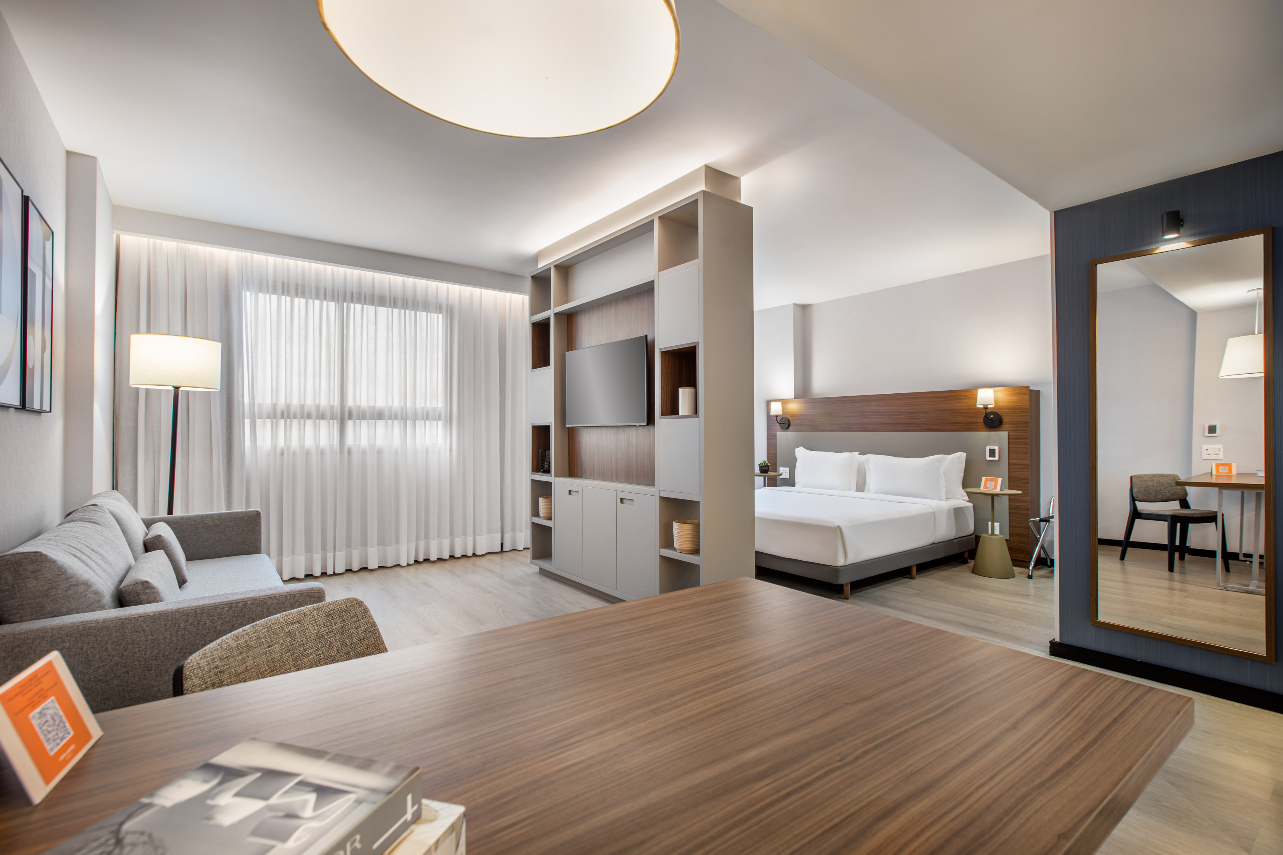 Bright modern hotel studio featuring living area, bed, and room divider with TV.