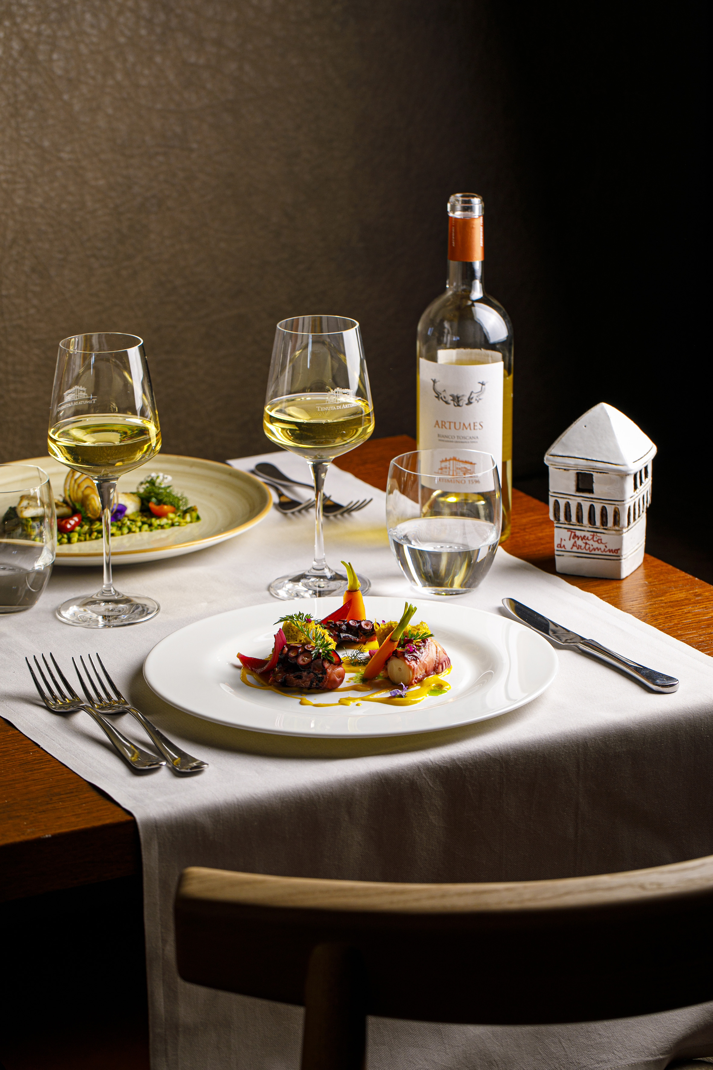 Gourmet octopus dish and white wine on an elegant restaurant table setting.