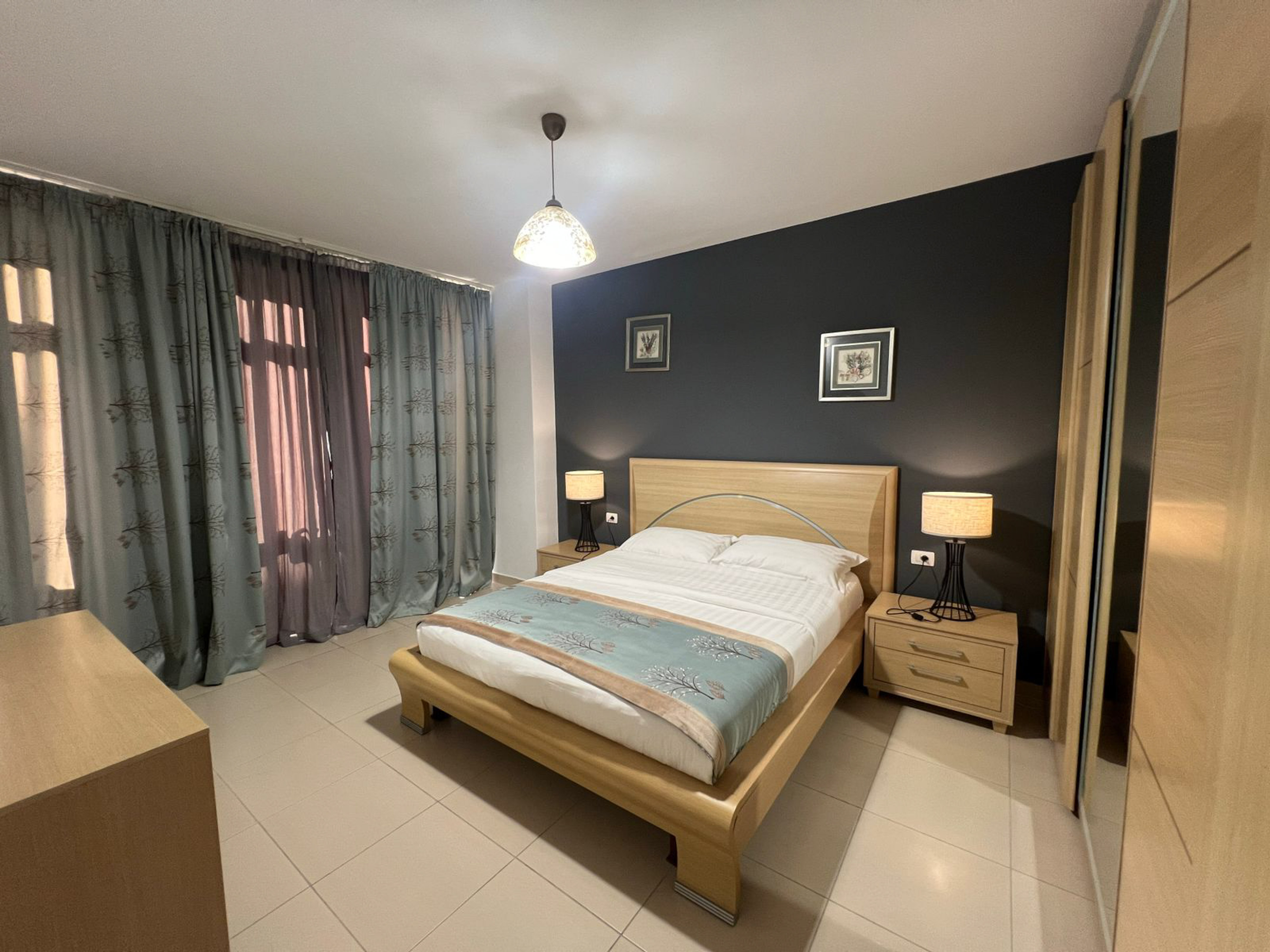 Modern double bedroom with wooden bed, dark accent wall, and patterned curtains.