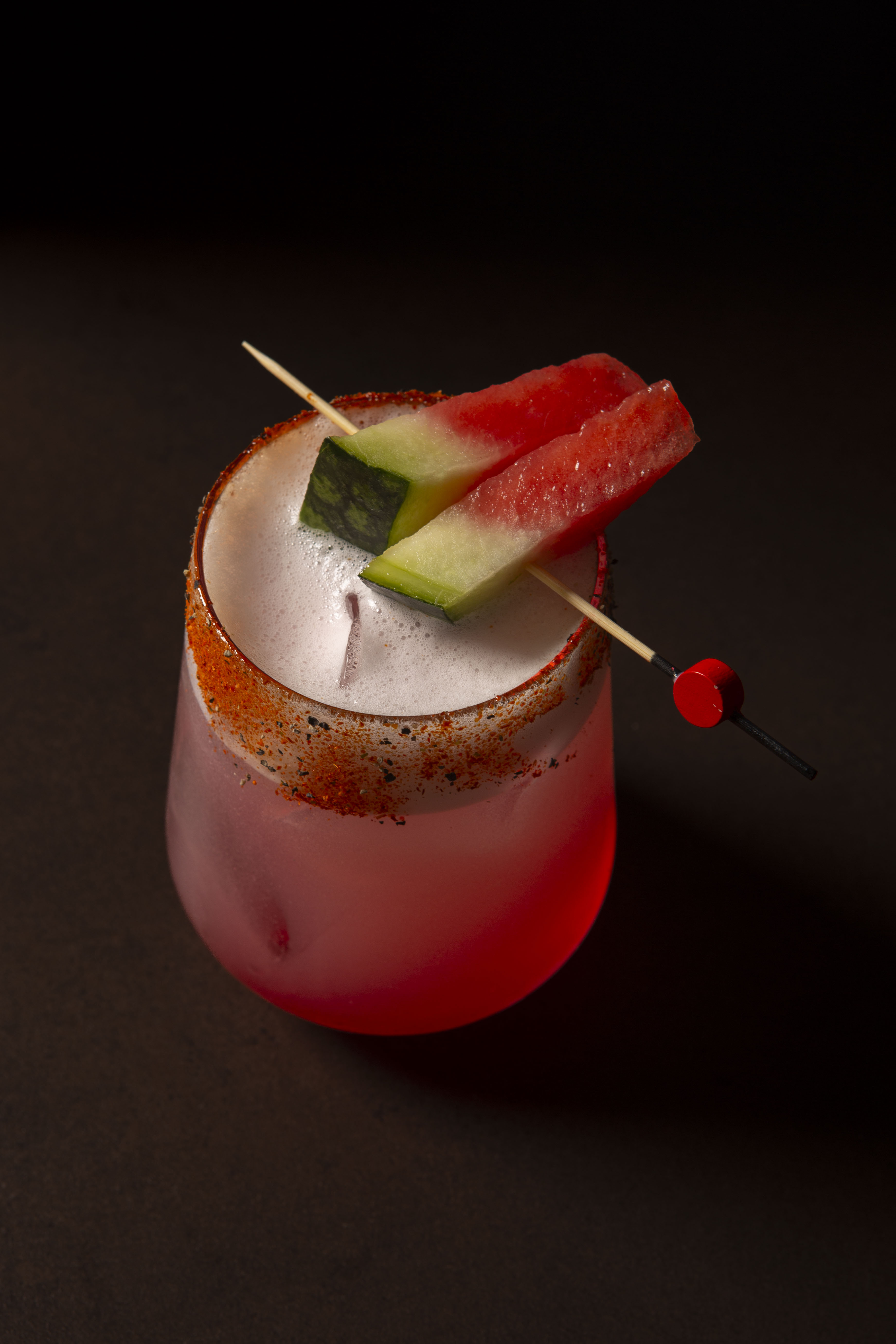Foamy pink watermelon cocktail with chili-spiced rim and melon slices.