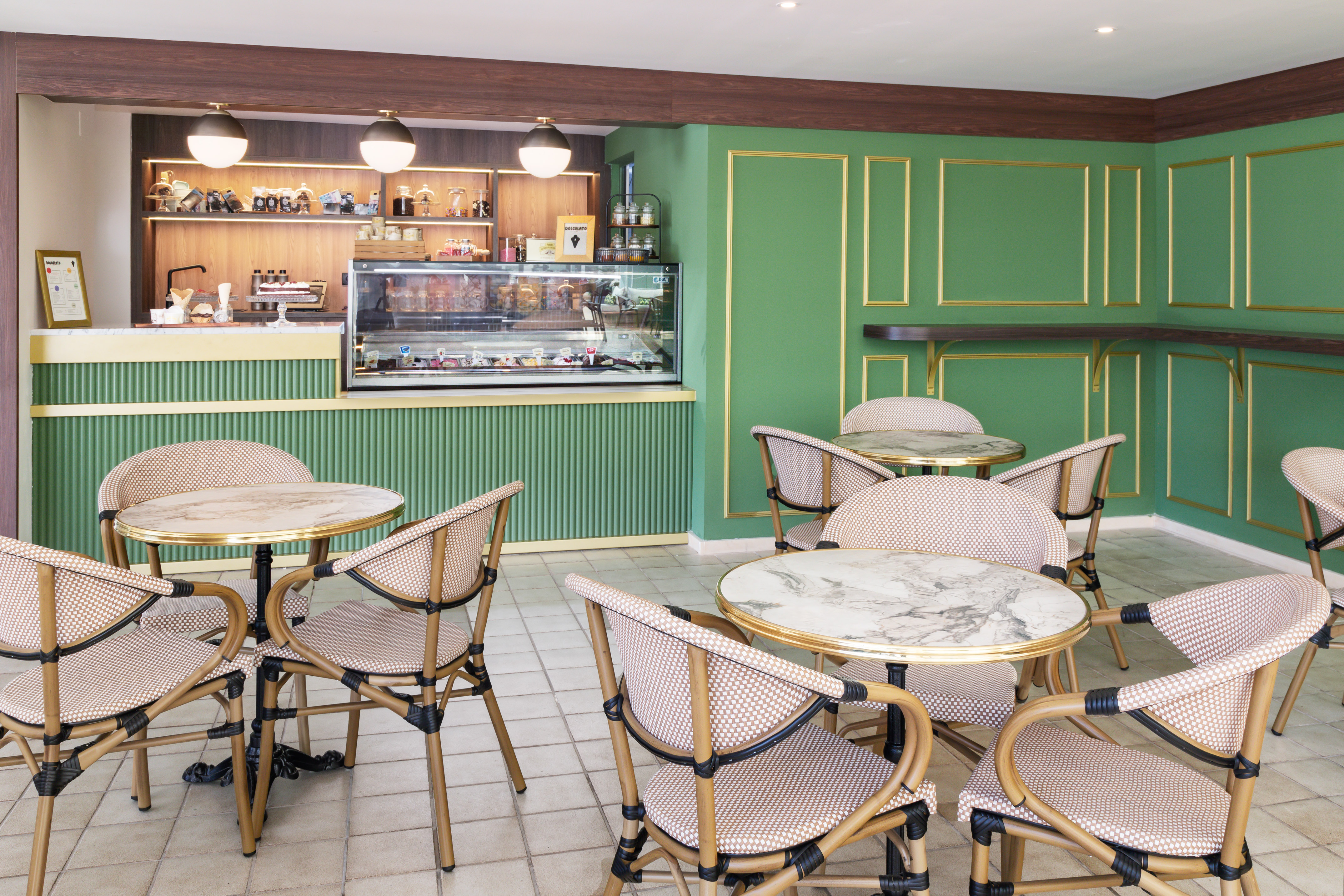 Cafe interior with green walls, gelato counter, marble tables, and wicker chairs.