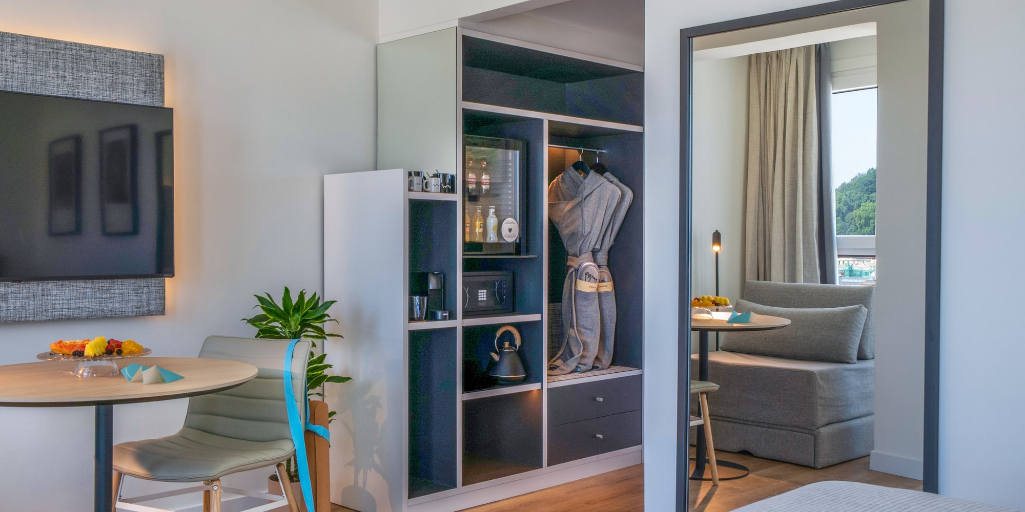 Suite de hotel moderna con minibar, armario, TV y zona de estar con vista.