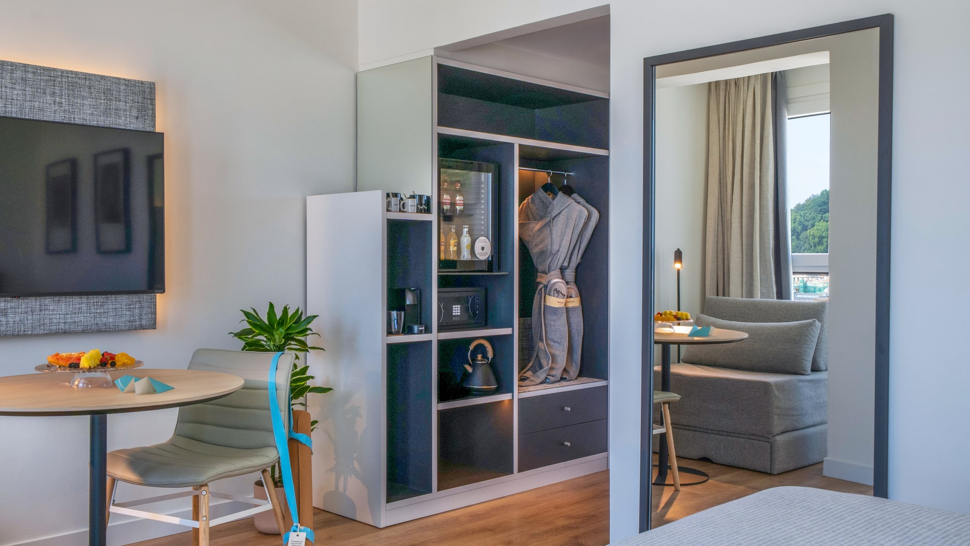 Suite de hotel moderna con minibar, armario, TV y zona de estar con vista.