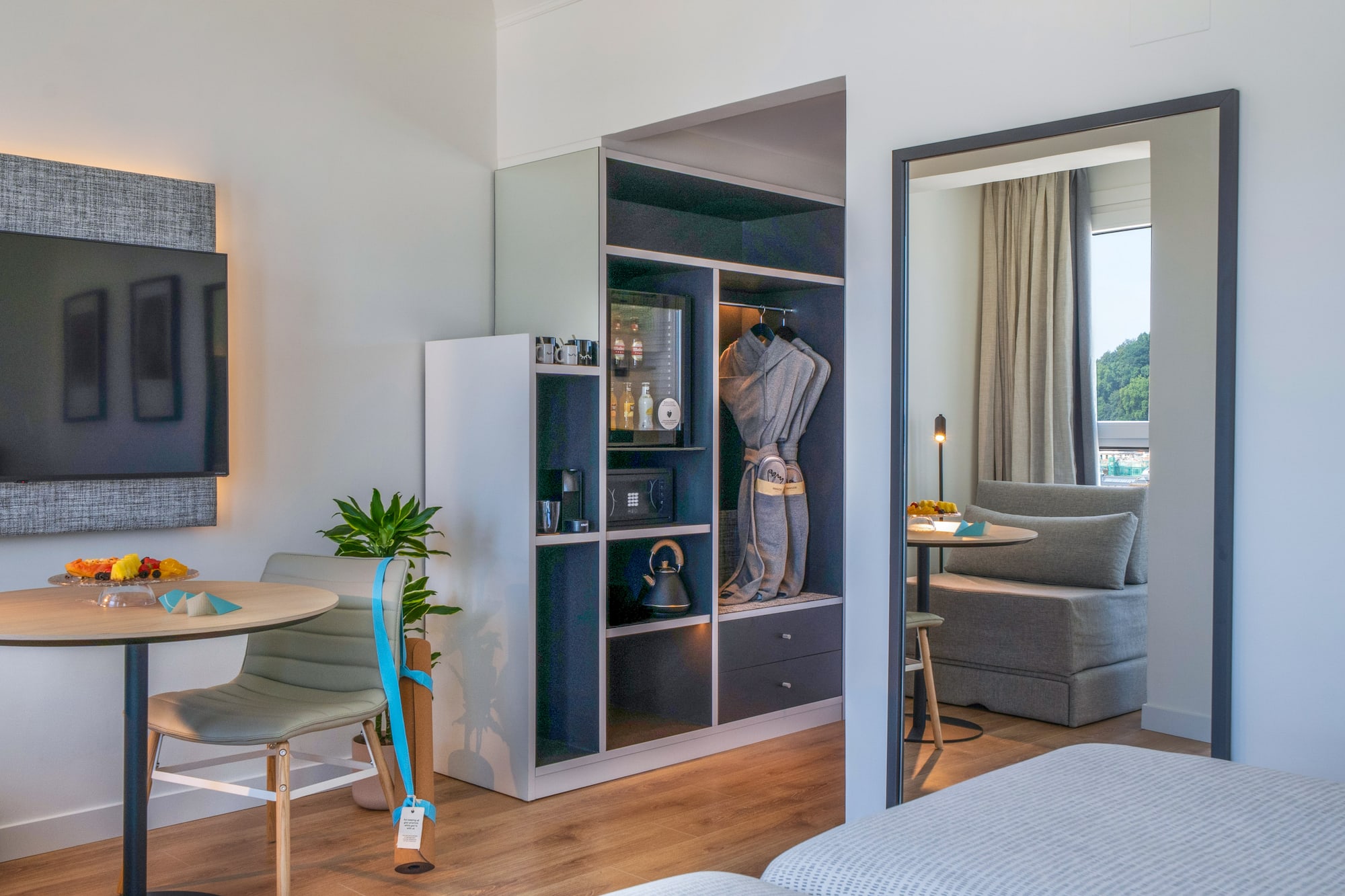 Suite de hotel moderna con minibar, armario, TV y zona de estar con vista.