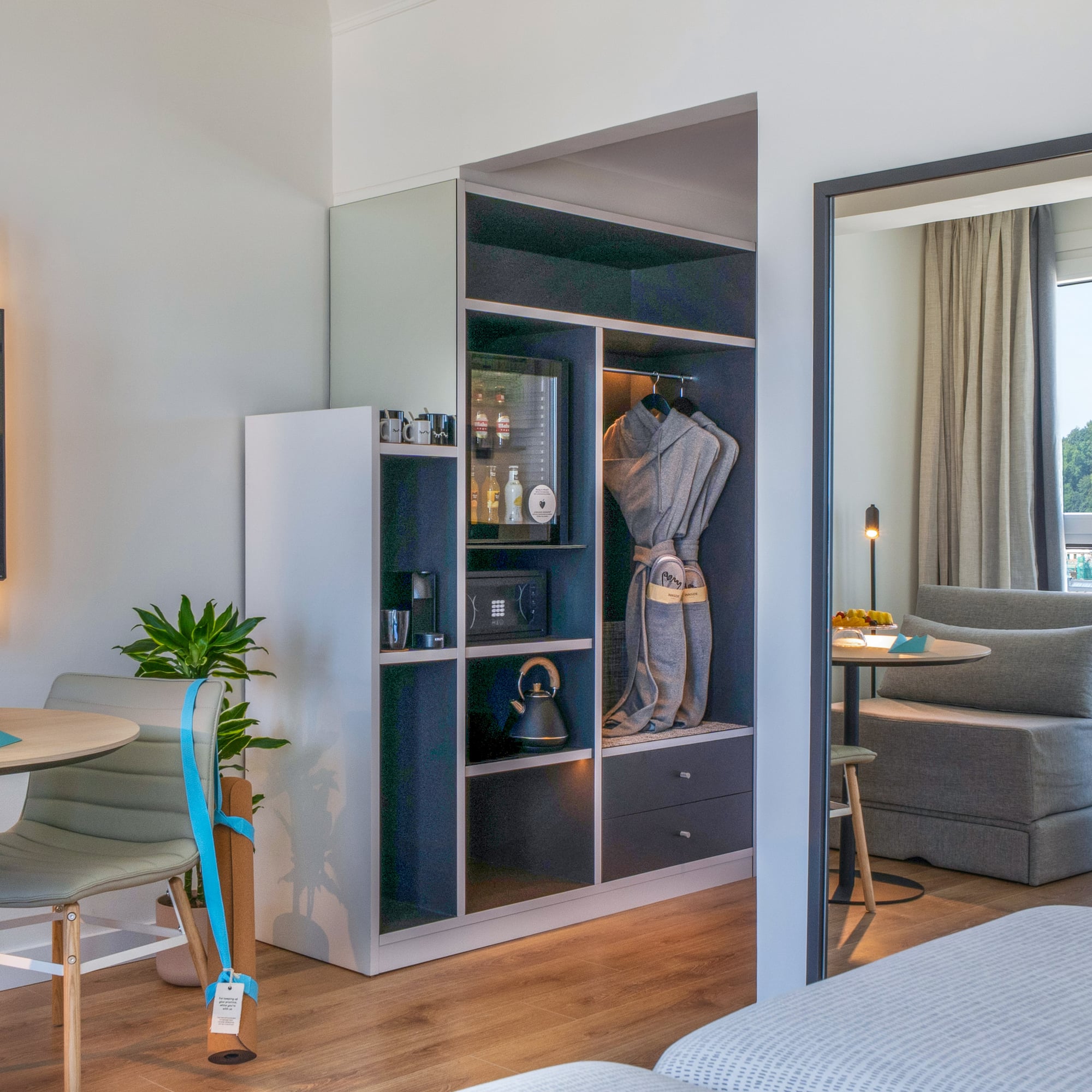 Suite de hotel moderna con minibar, armario, TV y zona de estar con vista.