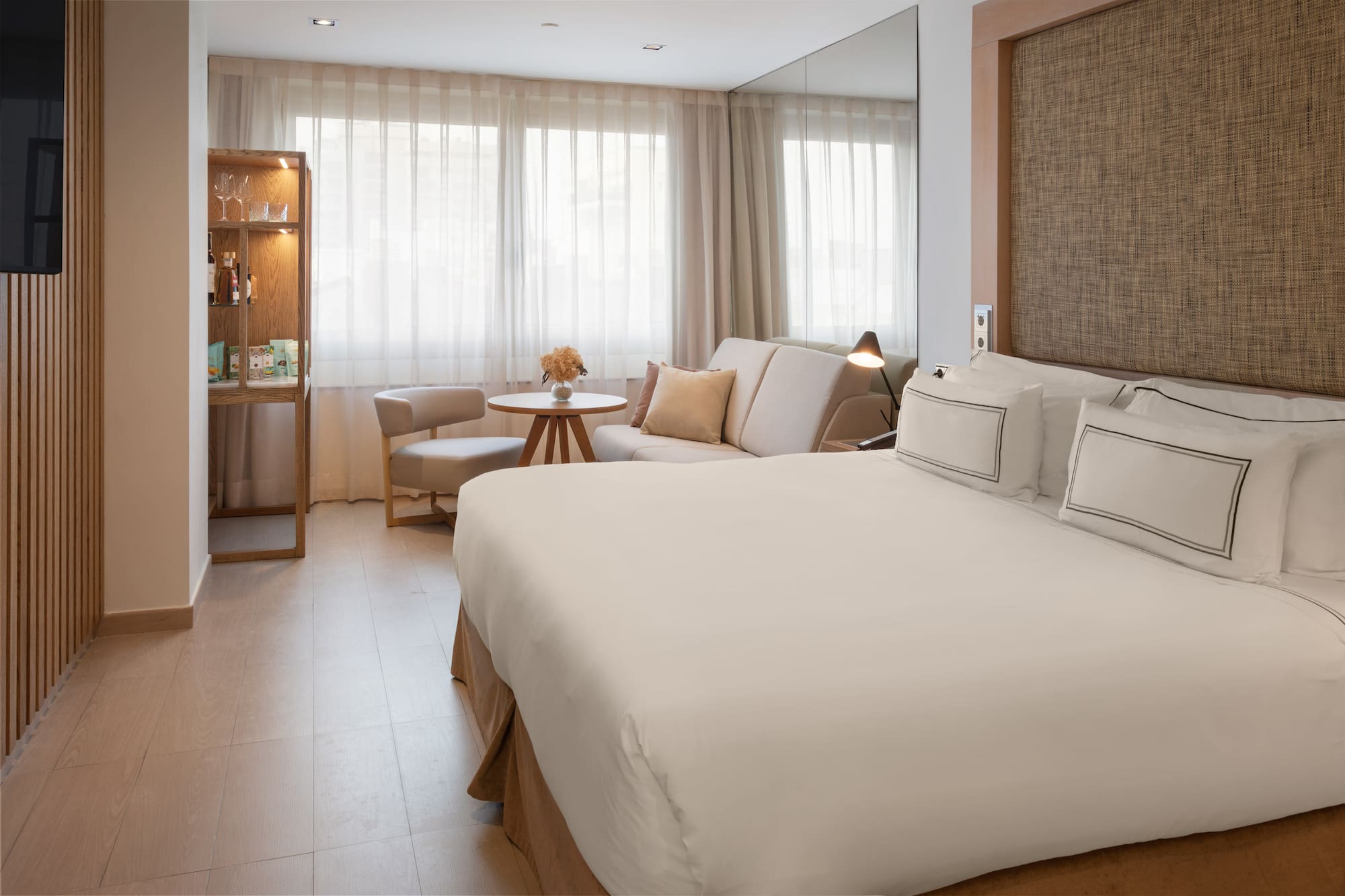 Bright hotel room with a large bed, sofa, and light wooden accents.