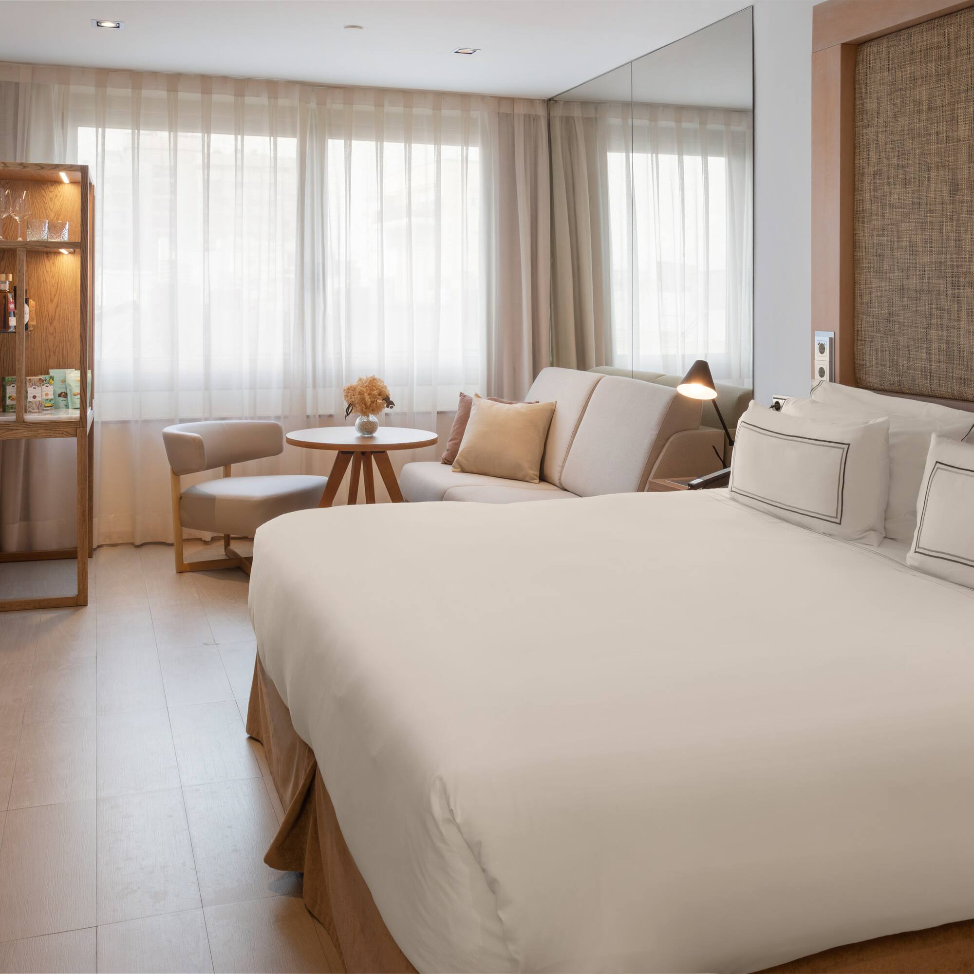 Bright hotel room with a large bed, sofa, and light wooden accents.