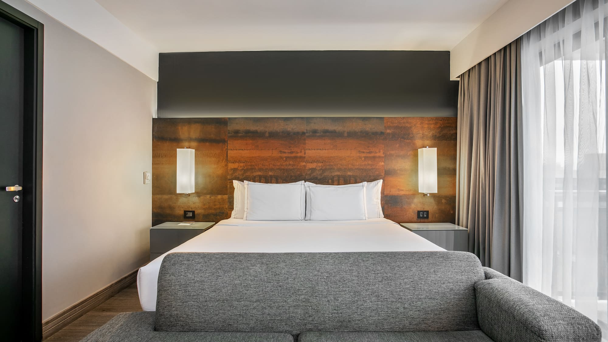 Quarto de hotel moderno com cama grande, cabeceira de metal e sofá cinza. - Deluxe Queen Room com Varanda - Meliá Ibirapuera, São Paulo