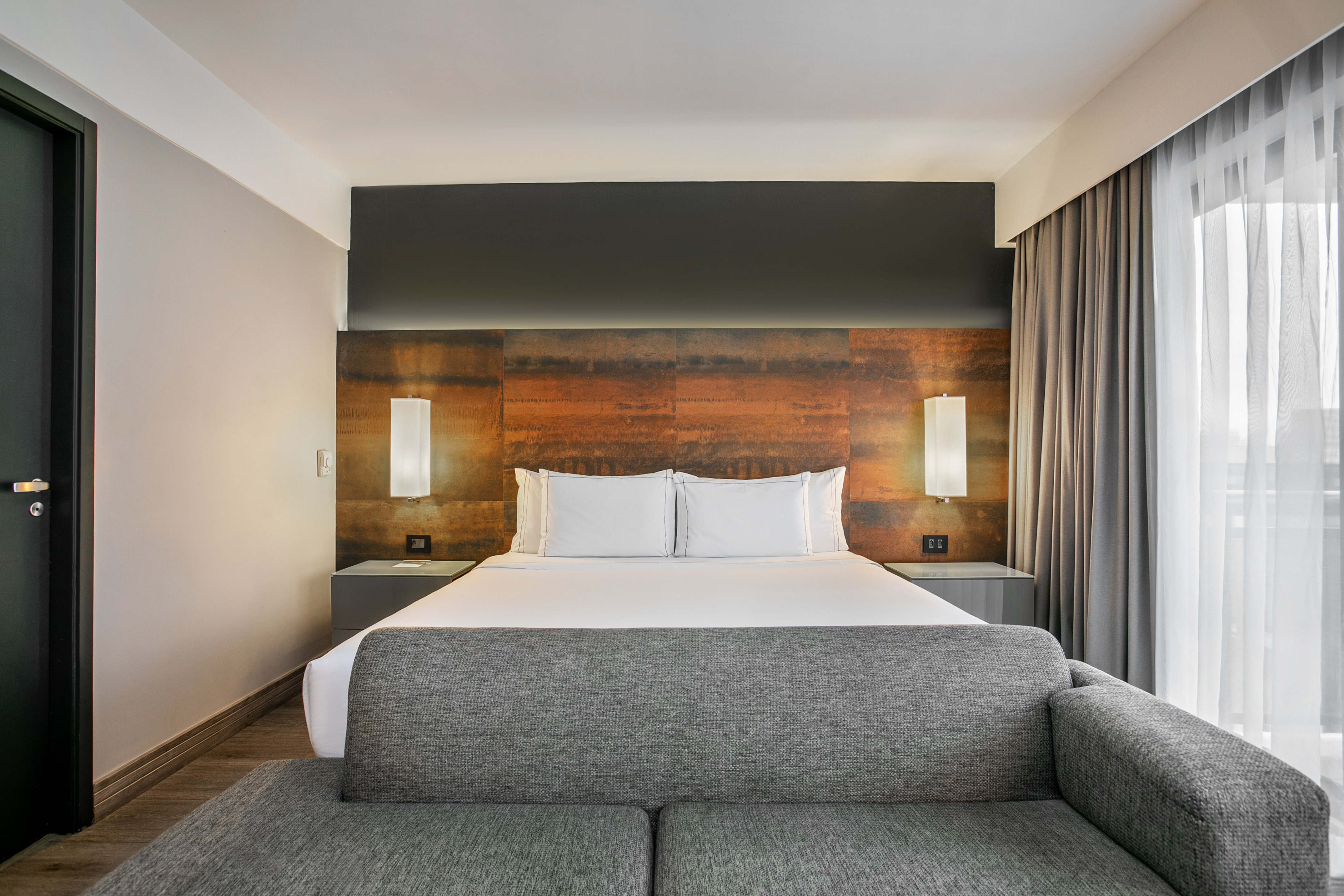 Quarto de hotel moderno com cama grande, cabeceira de metal e sofá cinza. - Deluxe Queen Room com Varanda - Meliá Ibirapuera, São Paulo