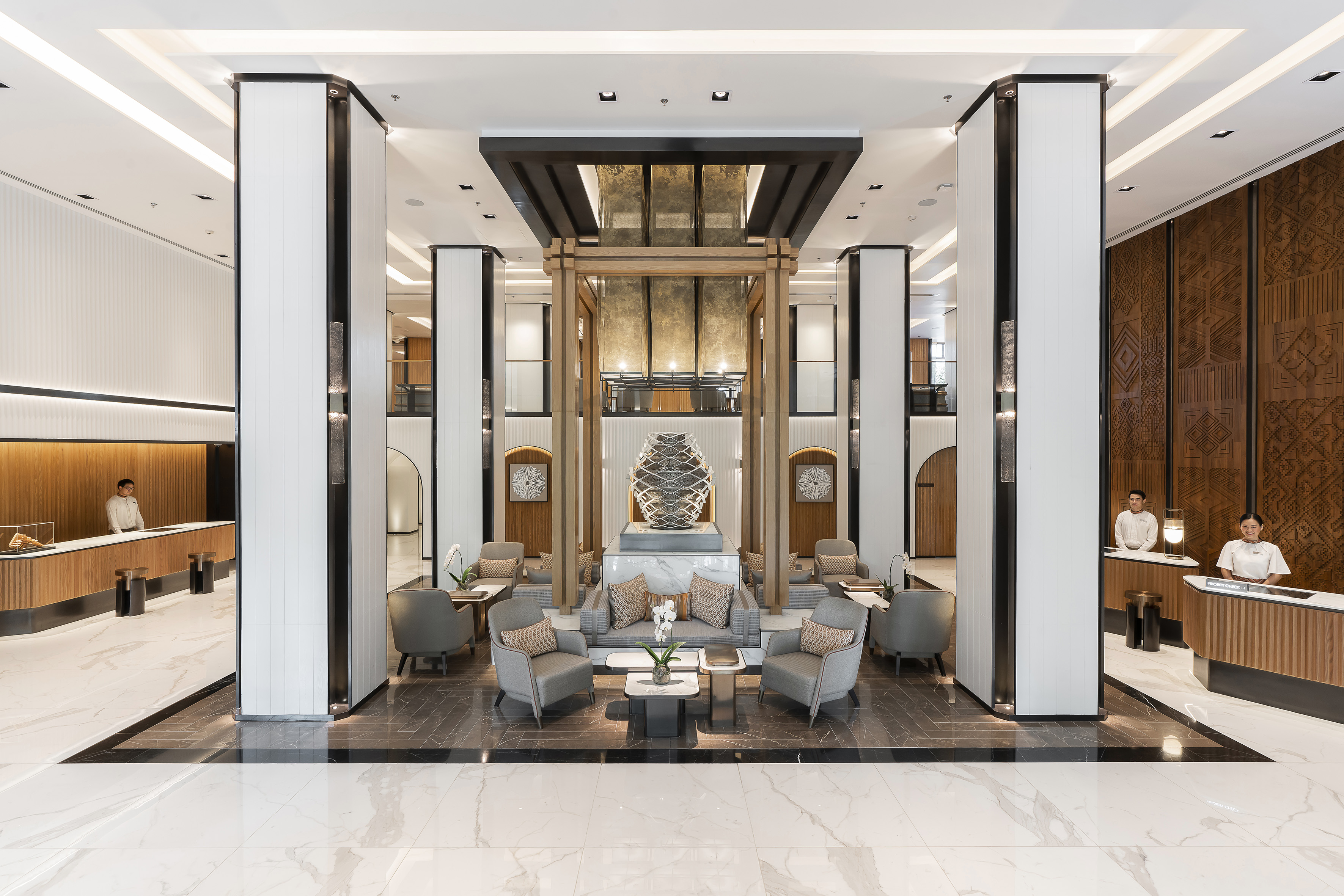 Modern hotel lobby with reception desks, central lounge seating, and art sculpture.