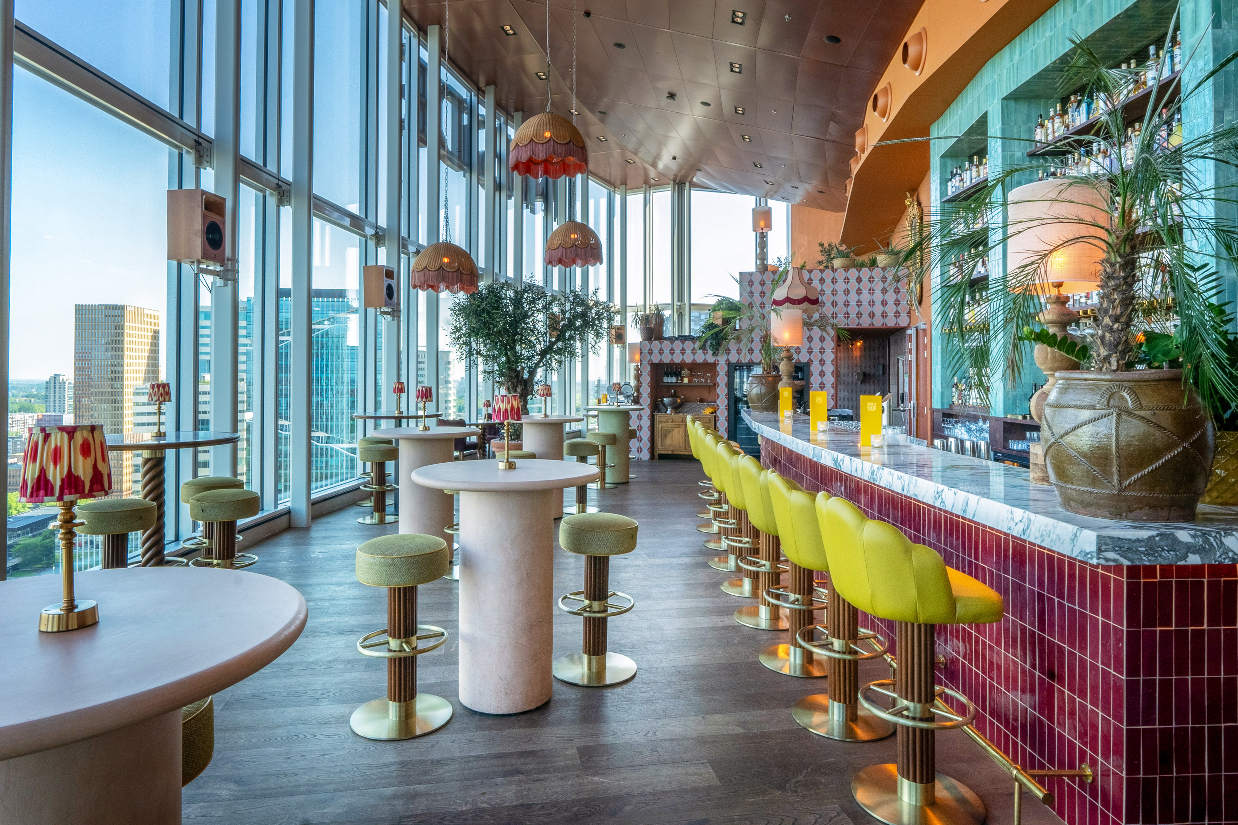 Vibrant rooftop bar with city view, yellow stools, and modern decor.