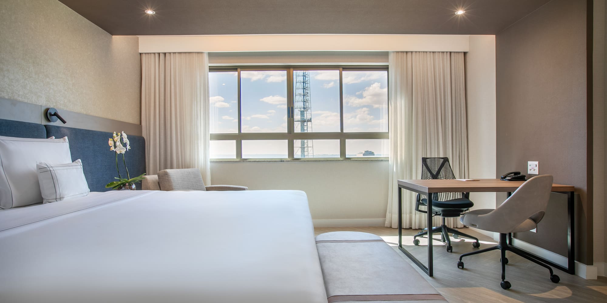 Modern hotel room with king bed, workstation, and city view.