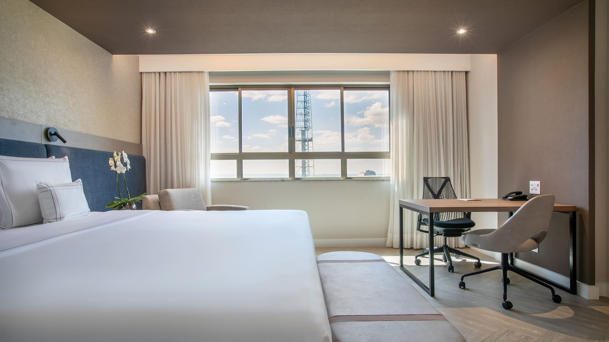 Modern hotel room with king bed, workstation, and city view.