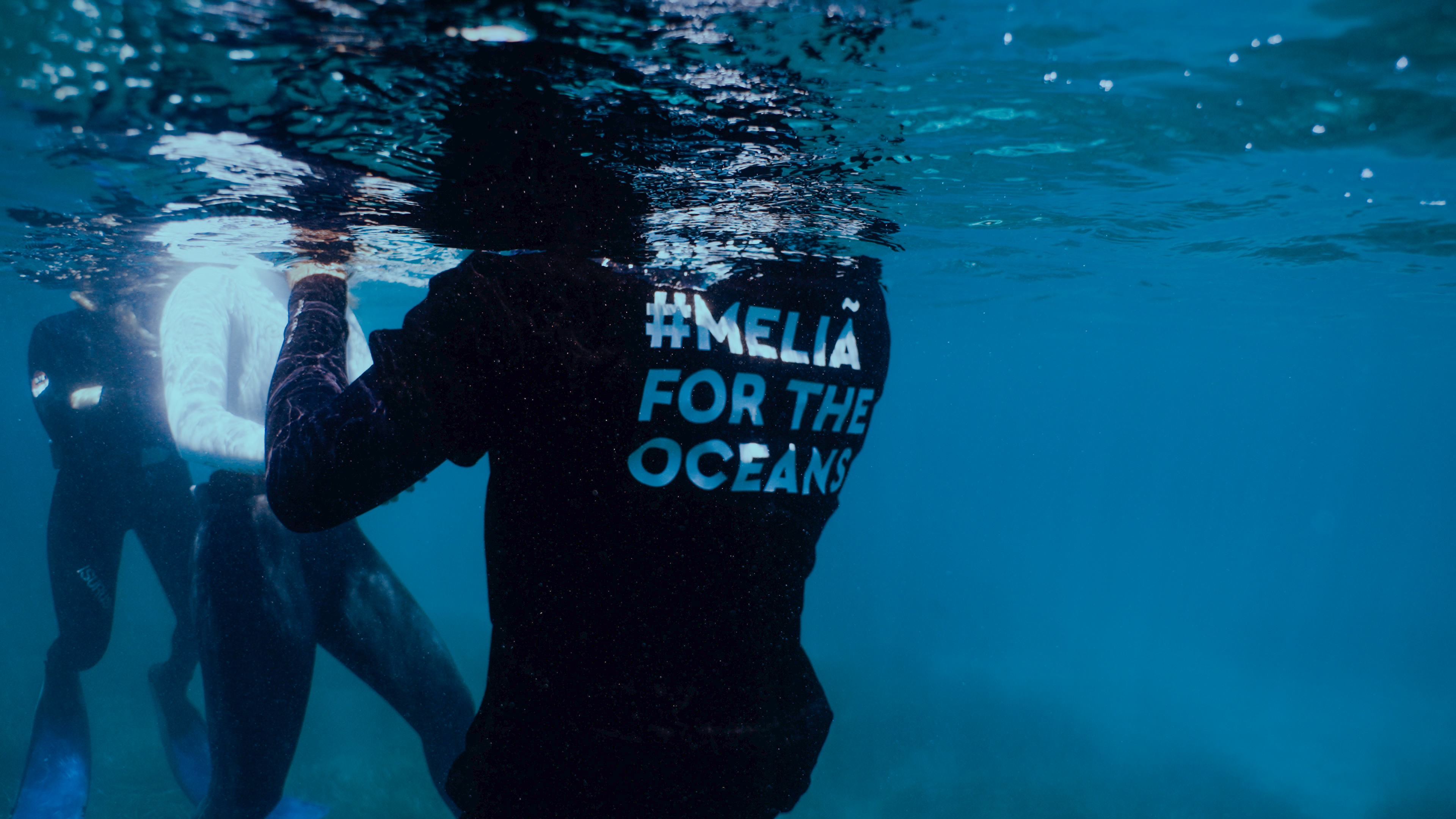 Ocean conservation swimmer in water with '#MELIÃ FOR THE OCEANS' shirt.