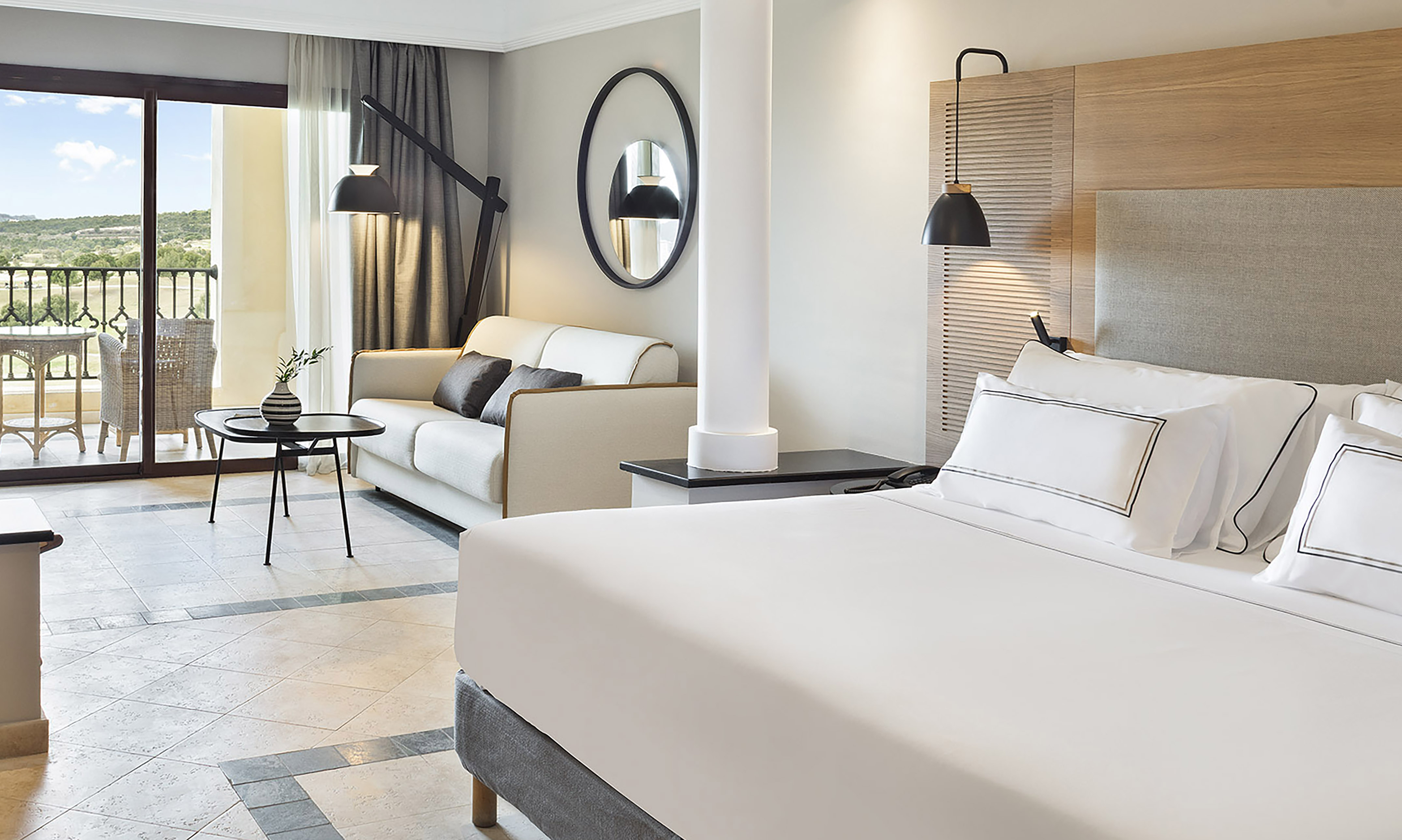 Luxury hotel suite with comfortable king bed, sofa, and scenic balcony view.