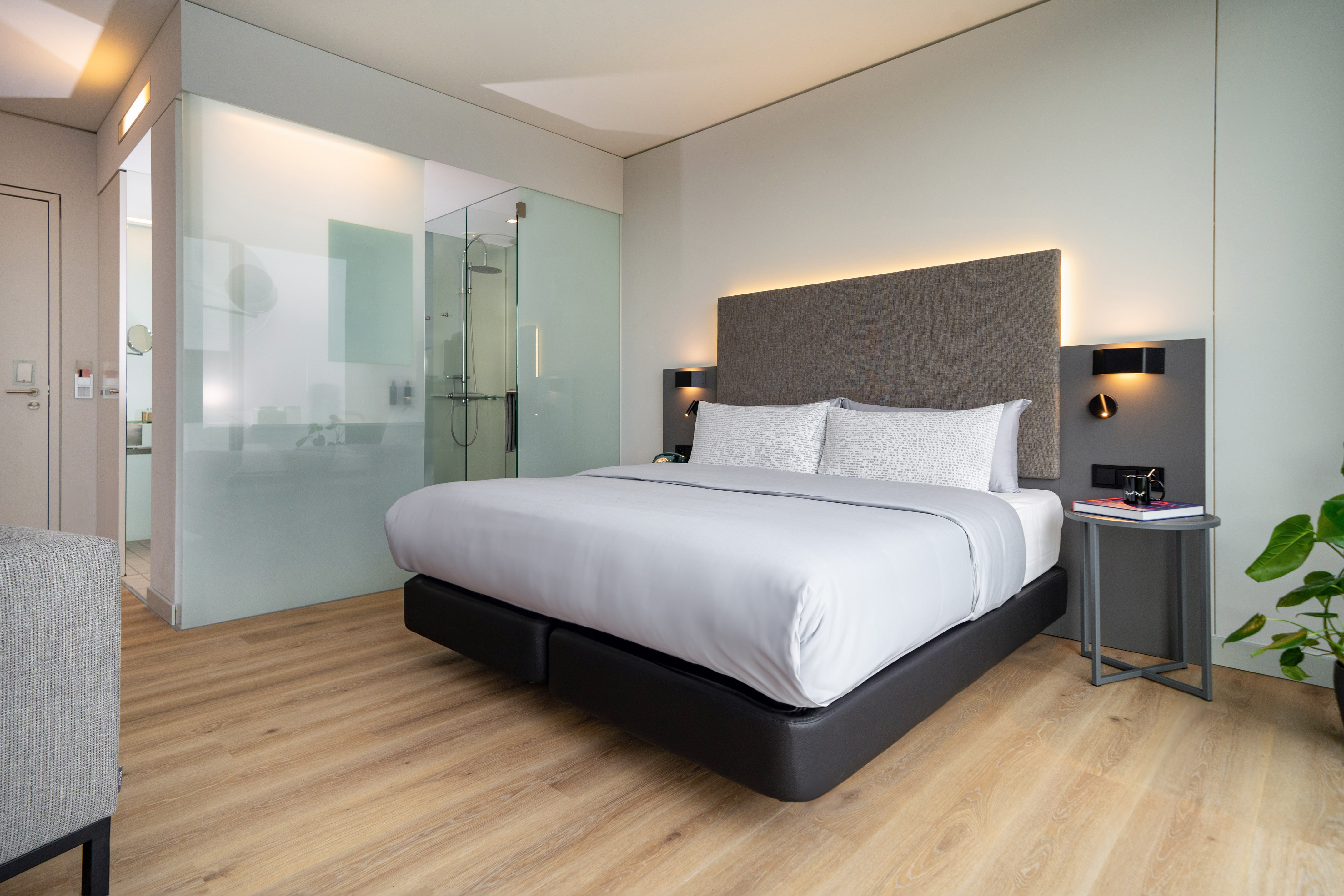 Modern hotel room with bed, wood floor, and glass shower partition.