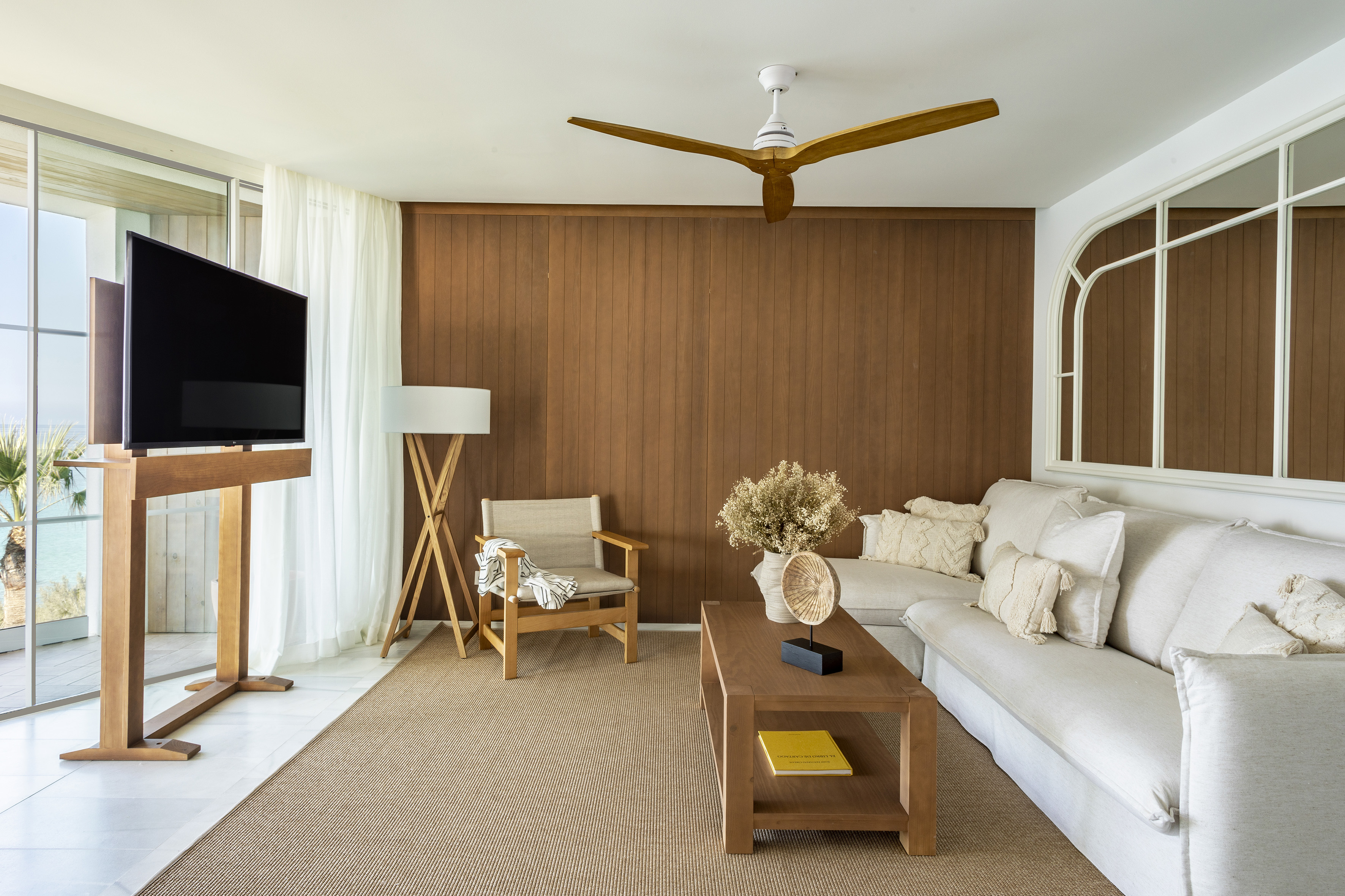 Modern beach house living room with wood paneling, white sofa, and sea view.
