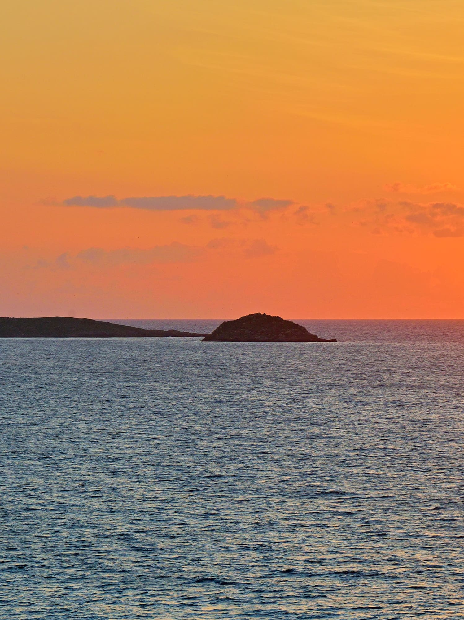 Orange sunset over ocean with bright sun and two islands.