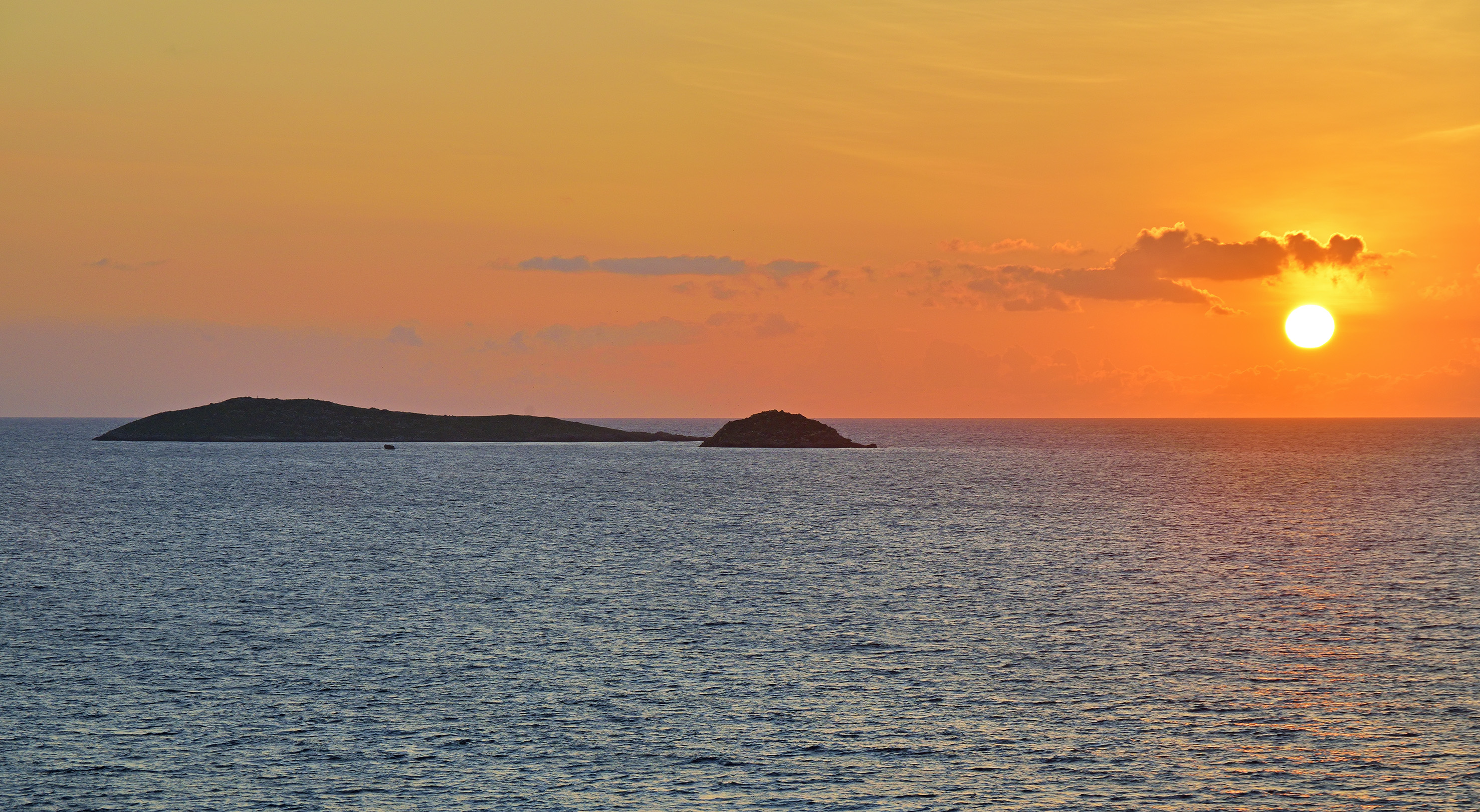 Sunset seascape with vibrant orange sky, islands, and bright sun.