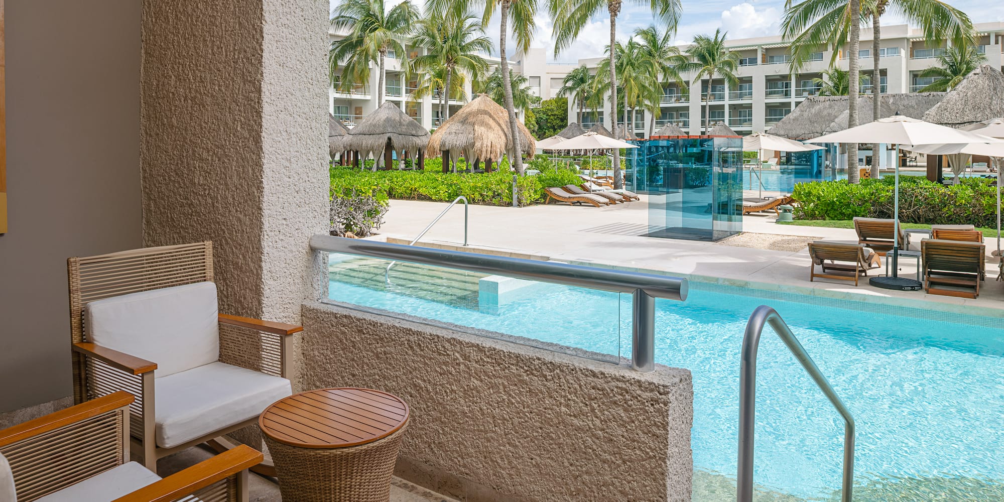 Hotel balcony with chairs, view of tropical pool, palm trees, and cabanas.