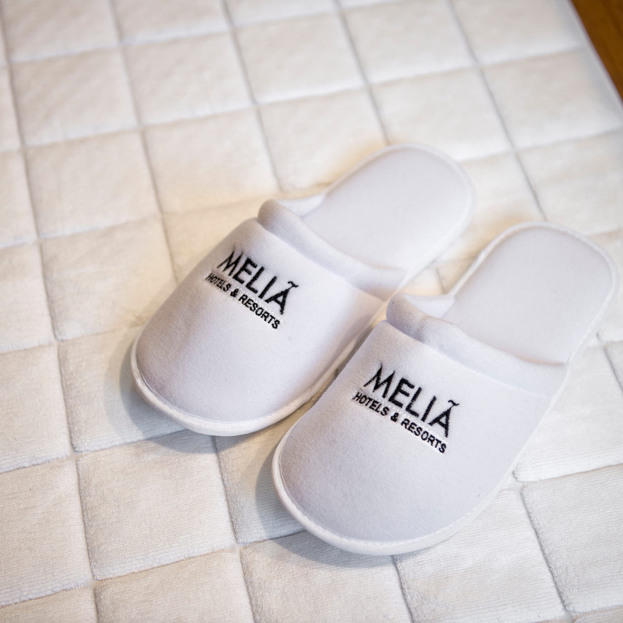 White Meliá Hotels & Resorts guest slippers on hotel bath mat.