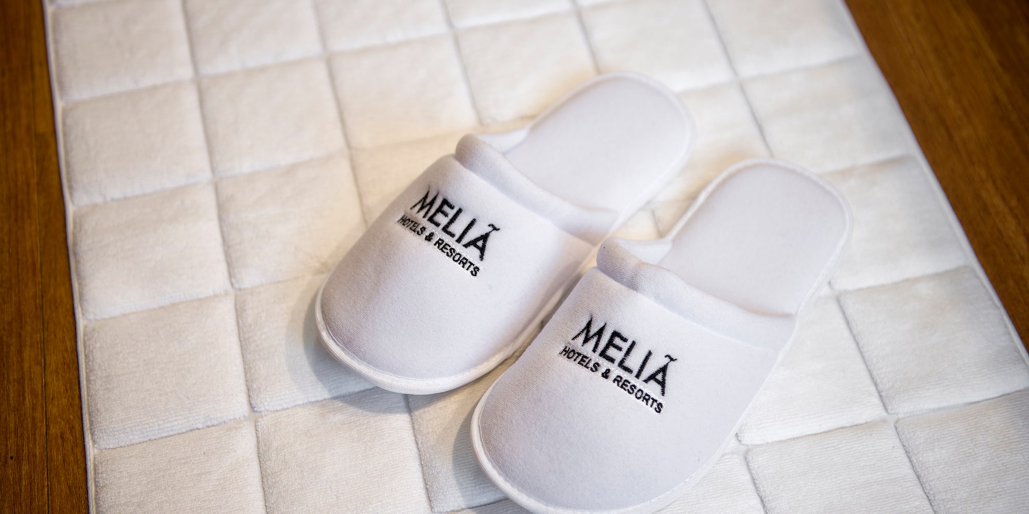 White Meliá Hotels & Resorts guest slippers on hotel bath mat.