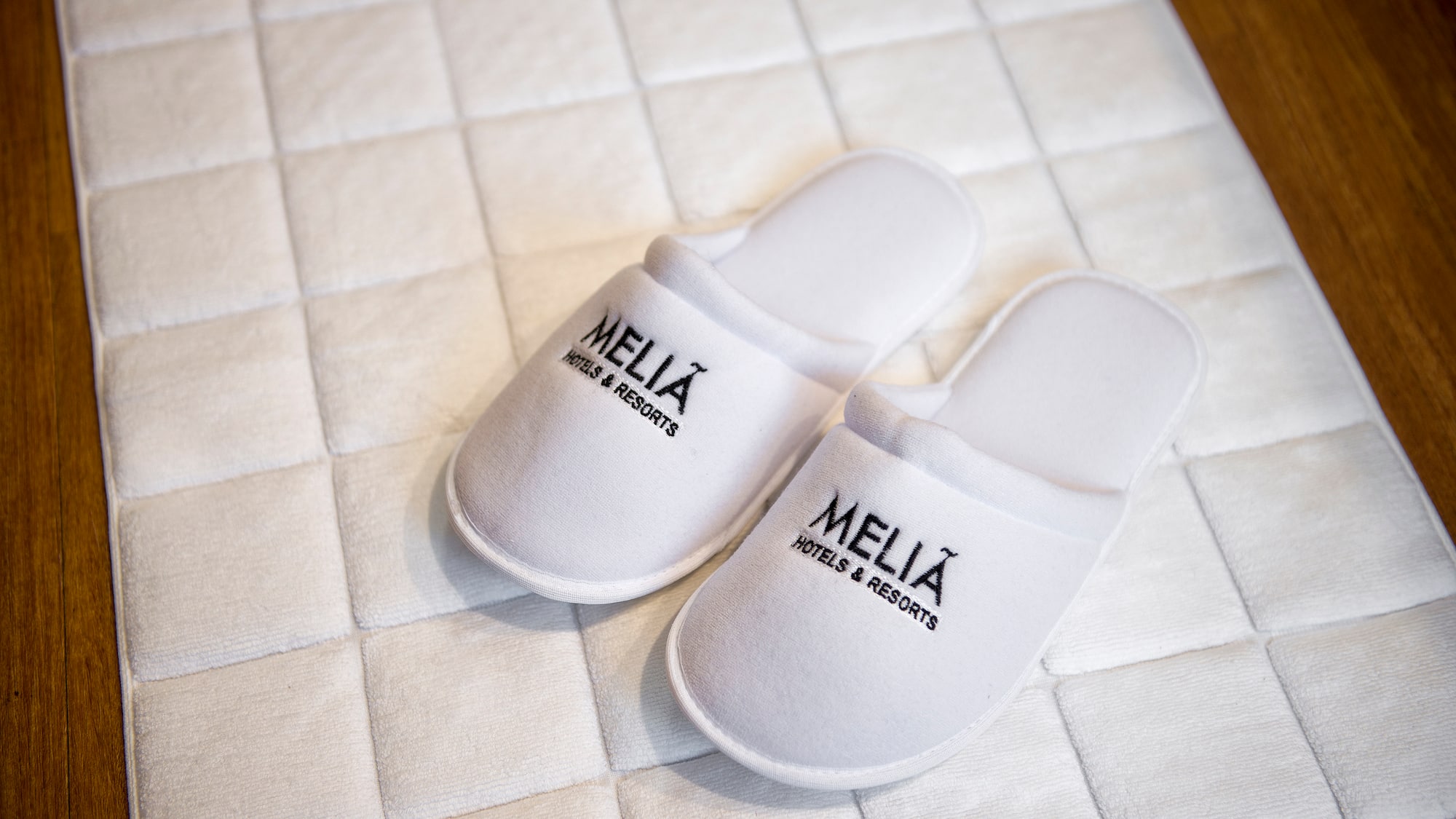 White Meliá Hotels & Resorts guest slippers on hotel bath mat.